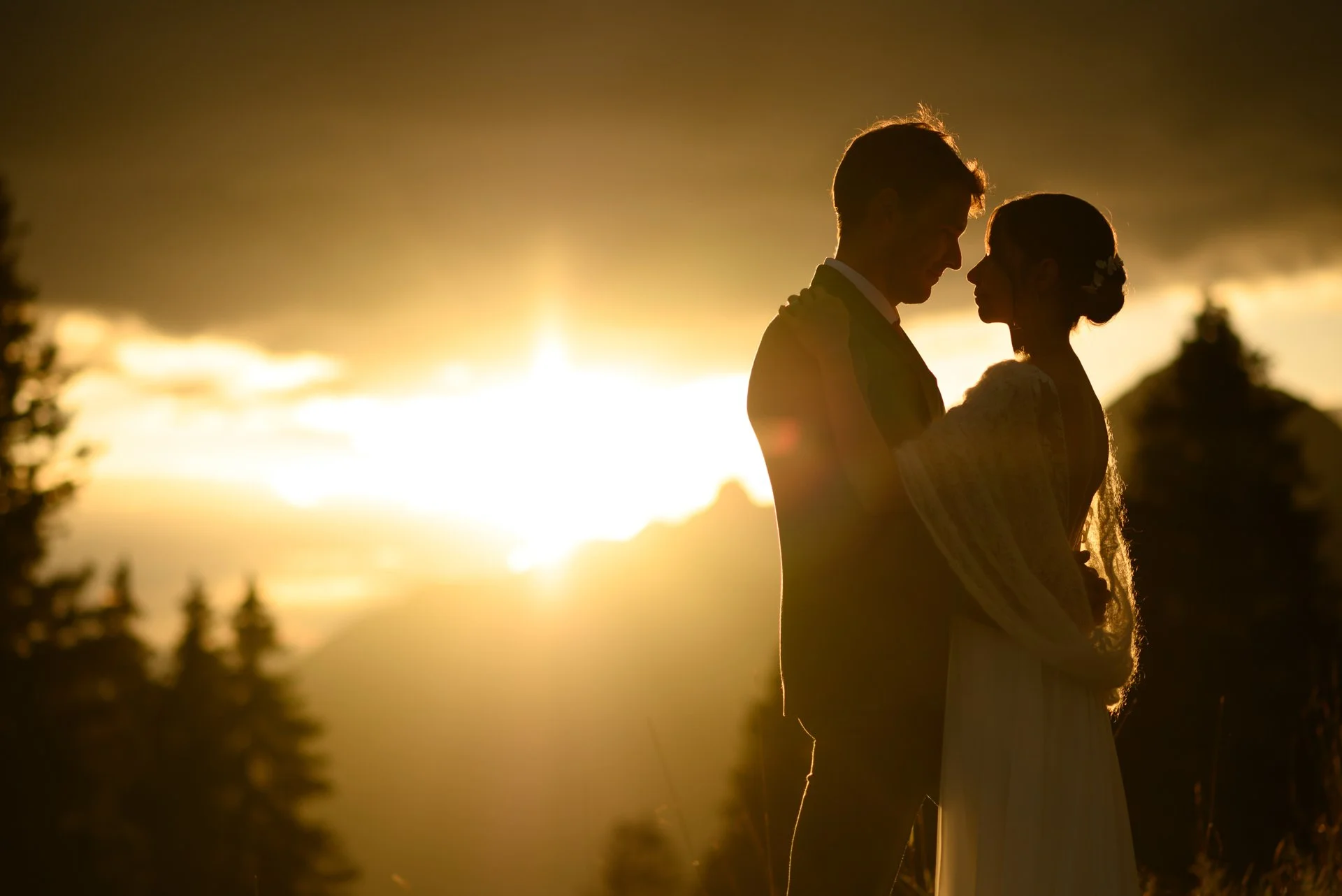 Un couple de mariés en silhouette regardant l'un l'autre au coucher du soleil, en plein air.