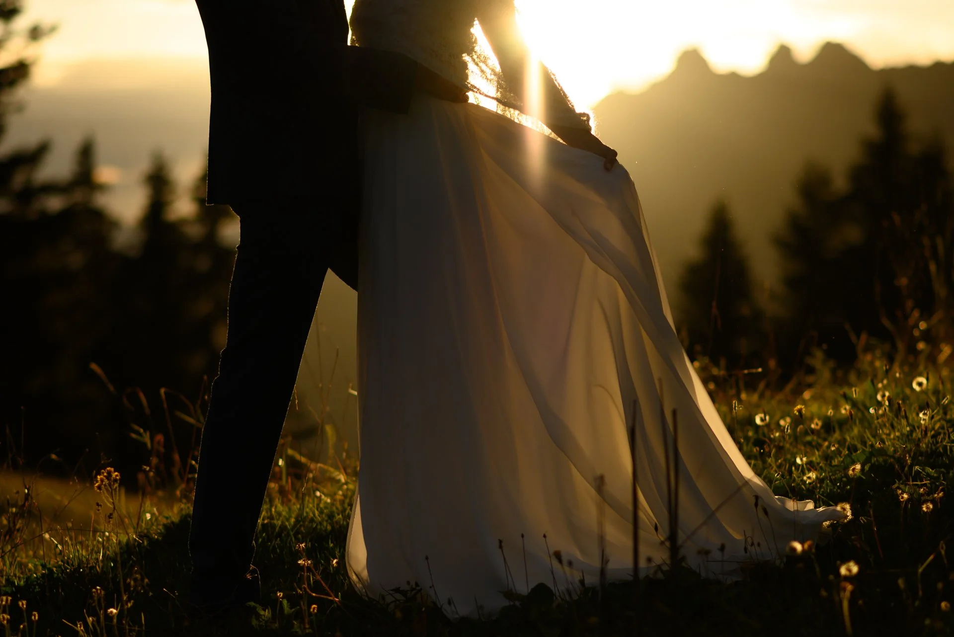 Un couple en mariage, vu en silhouette, se tenant dans un champ lors du coucher du soleil.