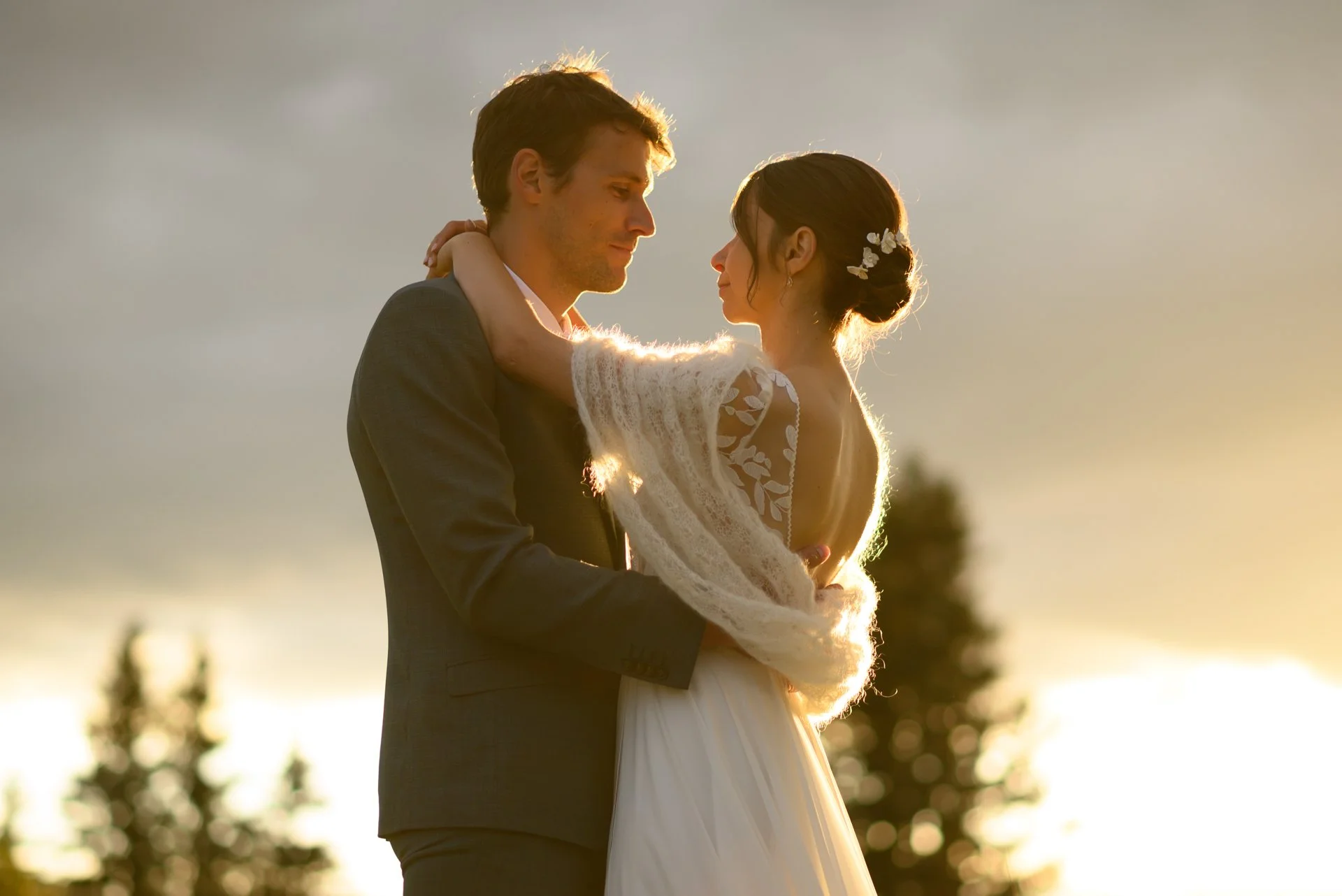Un couple en mariage se tenant par la taille sous un ciel au coucher du soleil, s'appréciant tendrement.