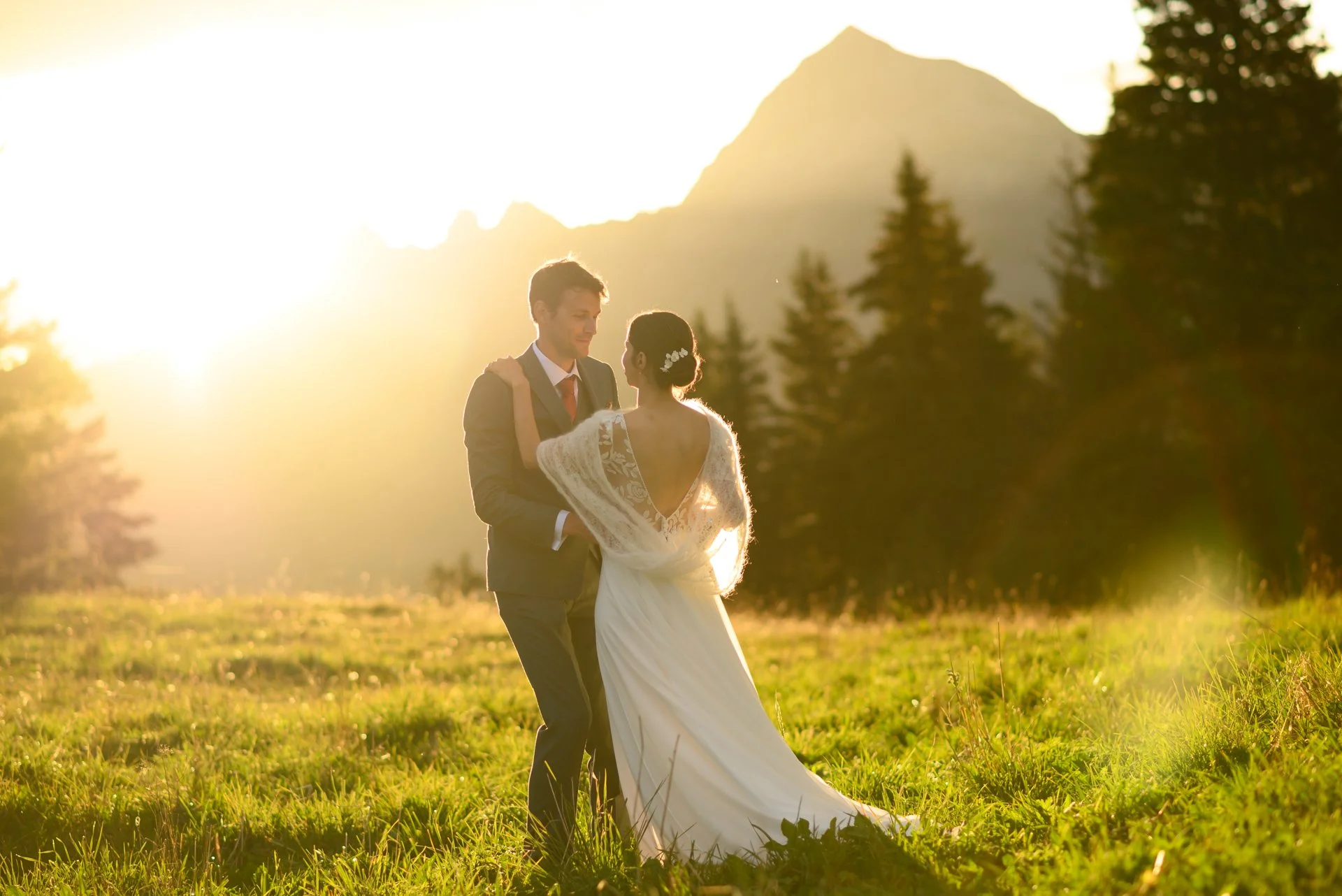 Un couple marié danse dans un champ en plein air au coucher du soleil, avec une montagne et des arbres en arrière-plan.