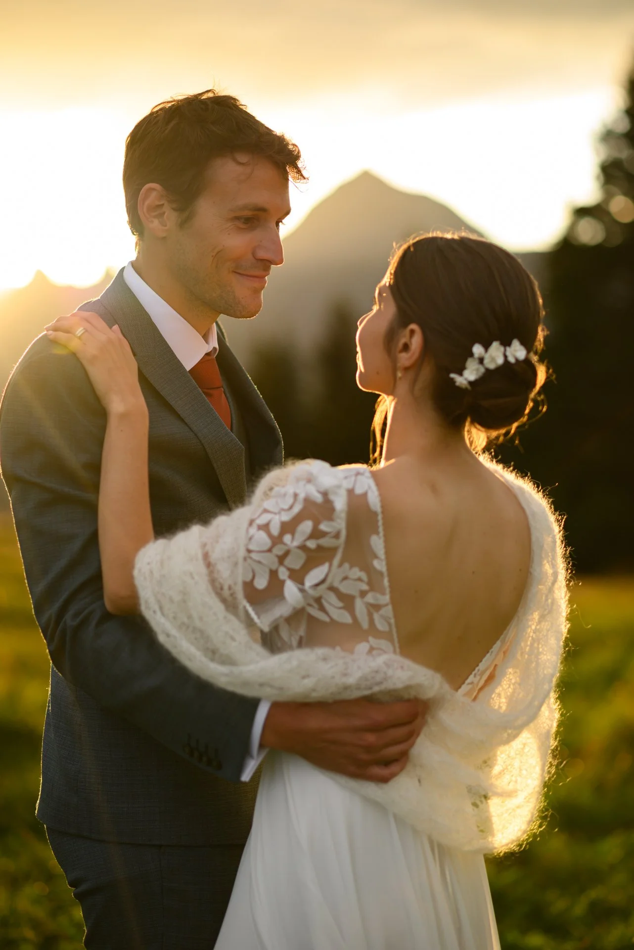 Un couple en robe de mariage et costume, se regardant avec tendresse lors d'une scène romantique au coucher du soleil dans un paysage naturel.