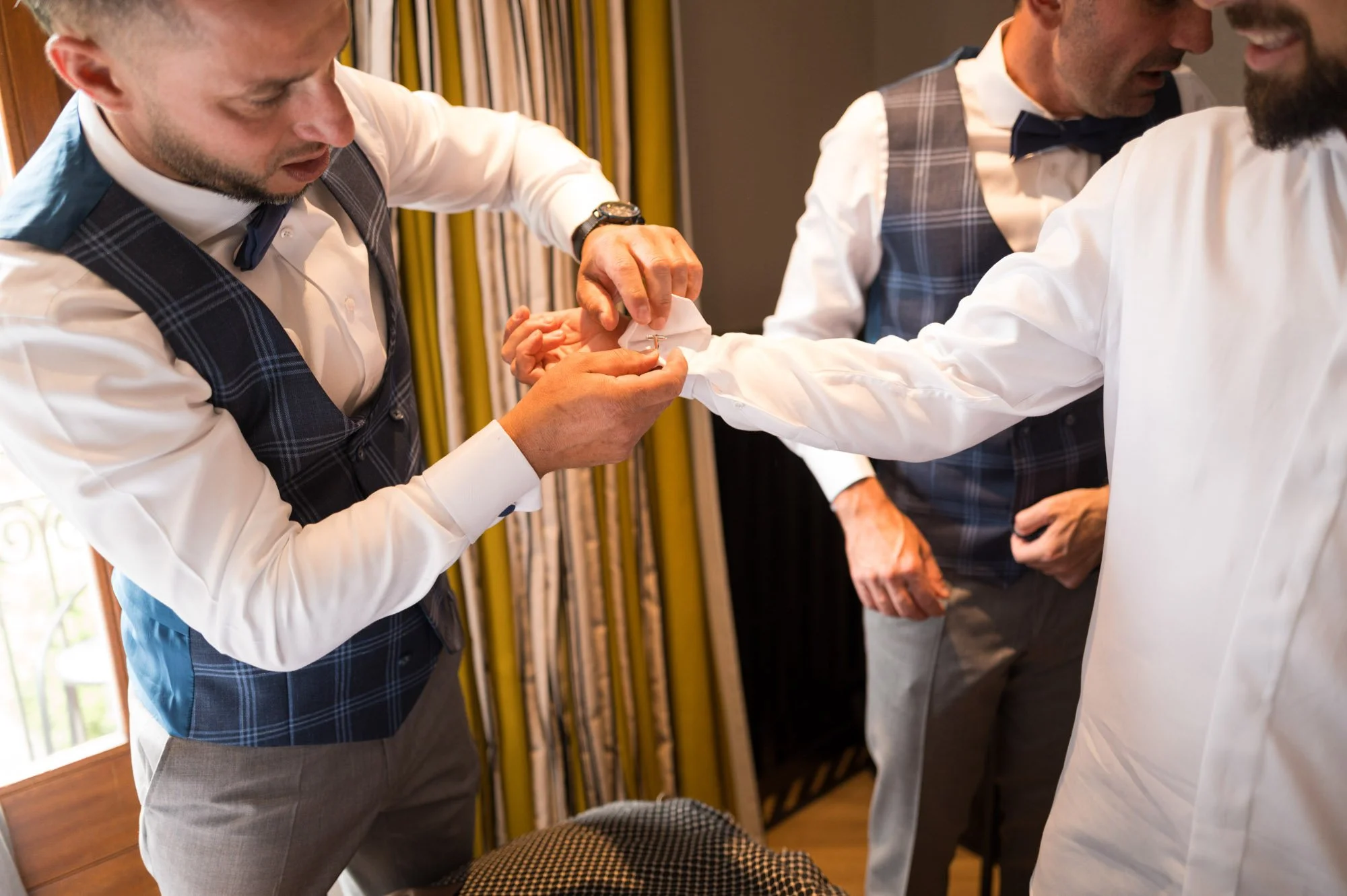 Trois hommes habillés en chemise et vestes de costume en train d'aider un autre homme à enfiler un manchon de manche de chemise.