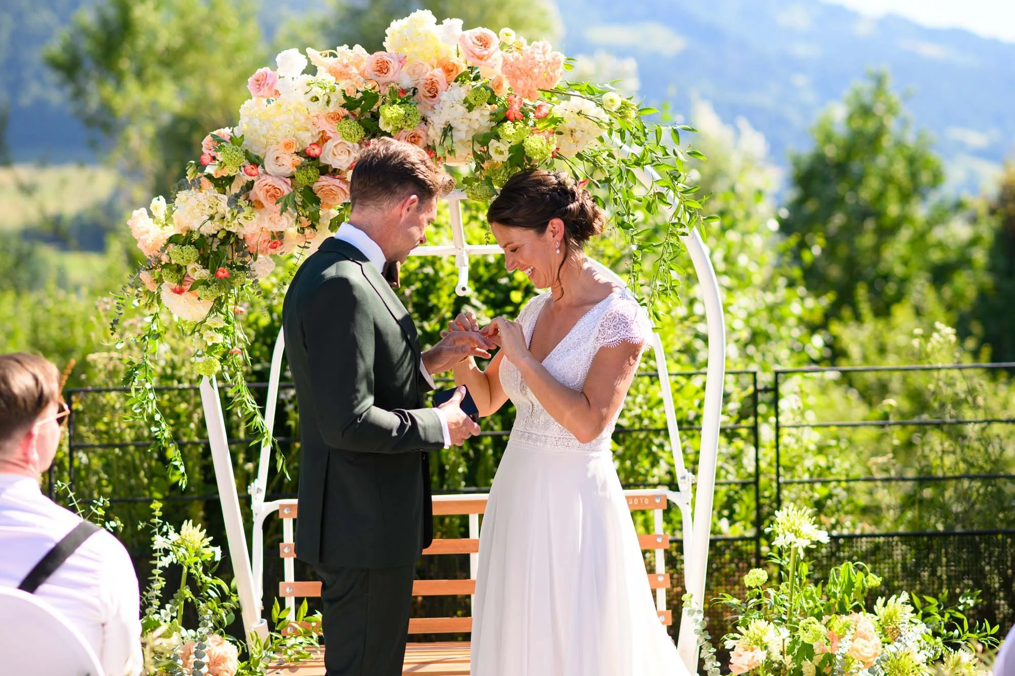 Un couple se mariant lors d'une cérémonie en plein air devant un décor floral coloré, en pleine nature.