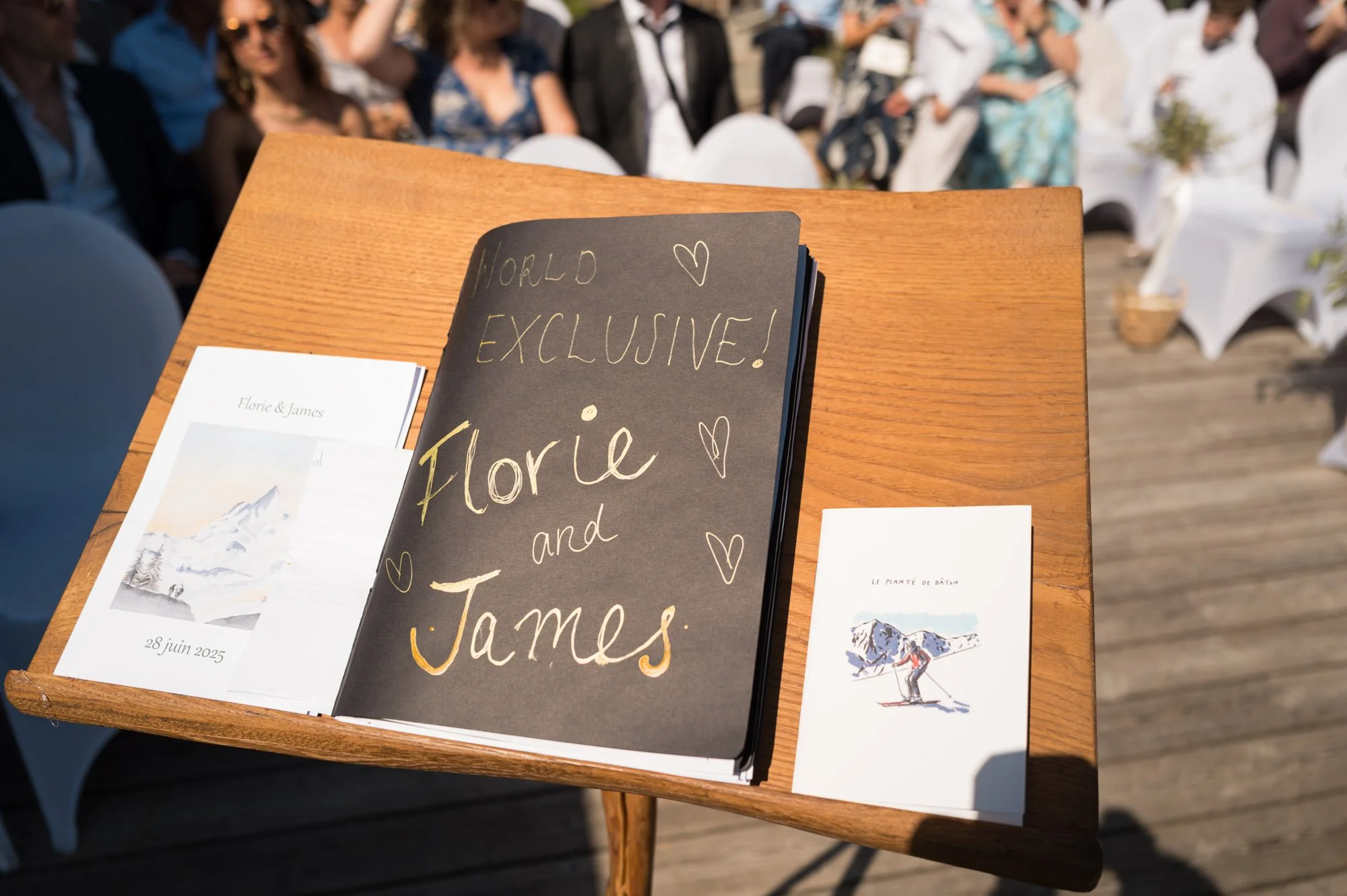 Livre d'or pour un mariage avec le nom "Florie et James" écrit à la craie, entouré par des invités assis à un mariage en plein air.