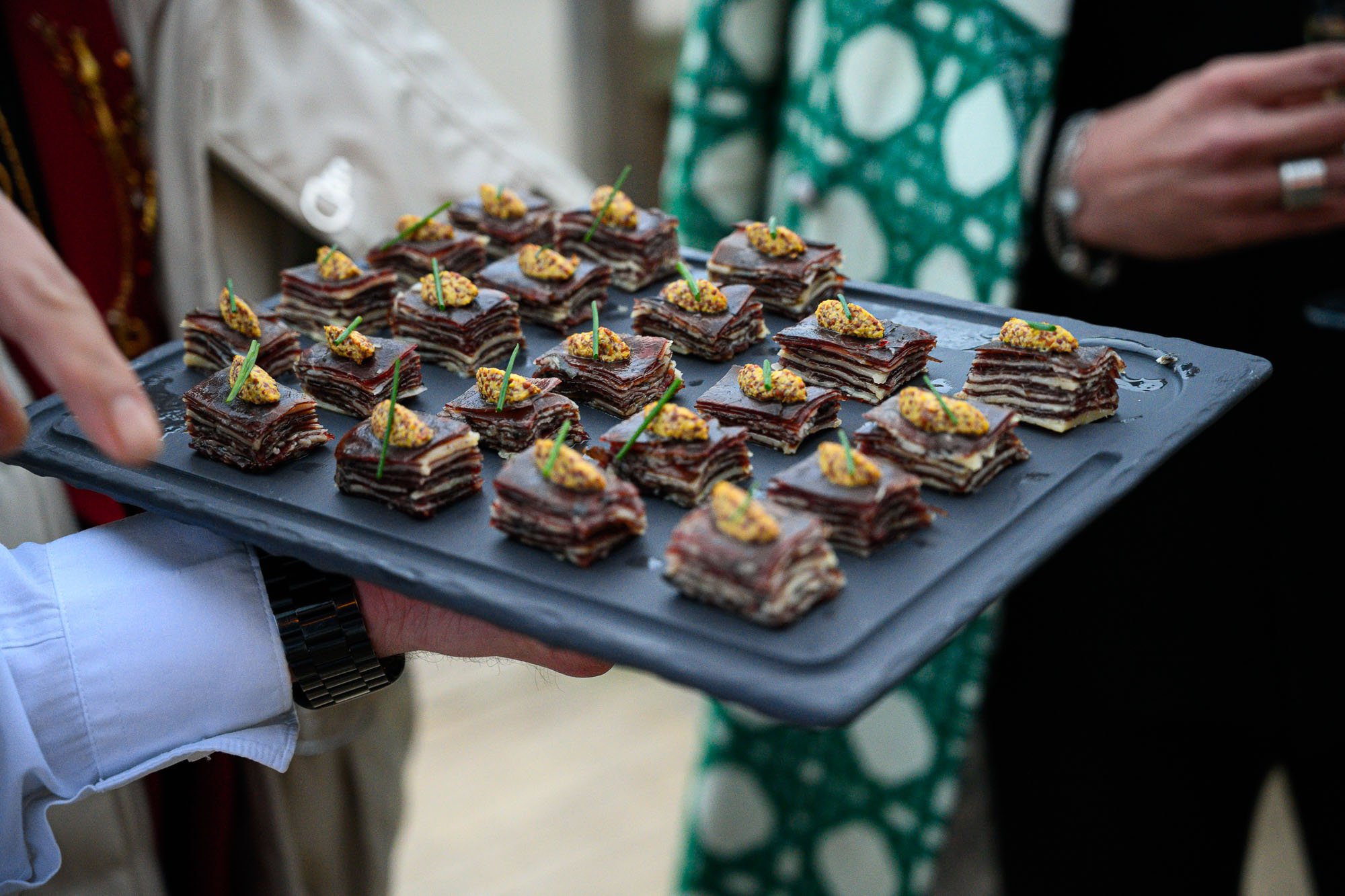 Plate de petits fours en forme de rectangles avec des couches multiples, décorés avec des petits morceaux d'amandes et des cure-dents avec des mini pliats.