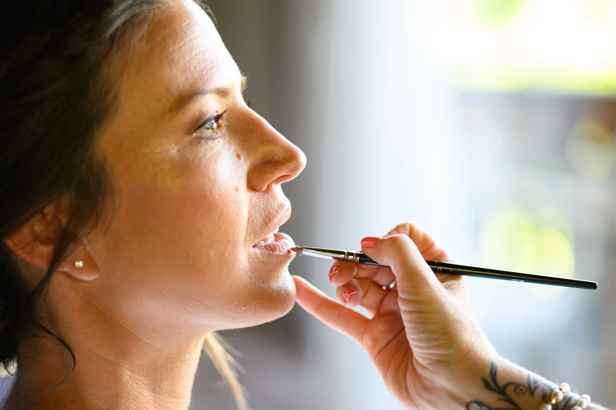 Une femme reçoit des soins de maquillage, un pinceau appliquant du rouge à lèvres ou du gloss sur ses lèvres