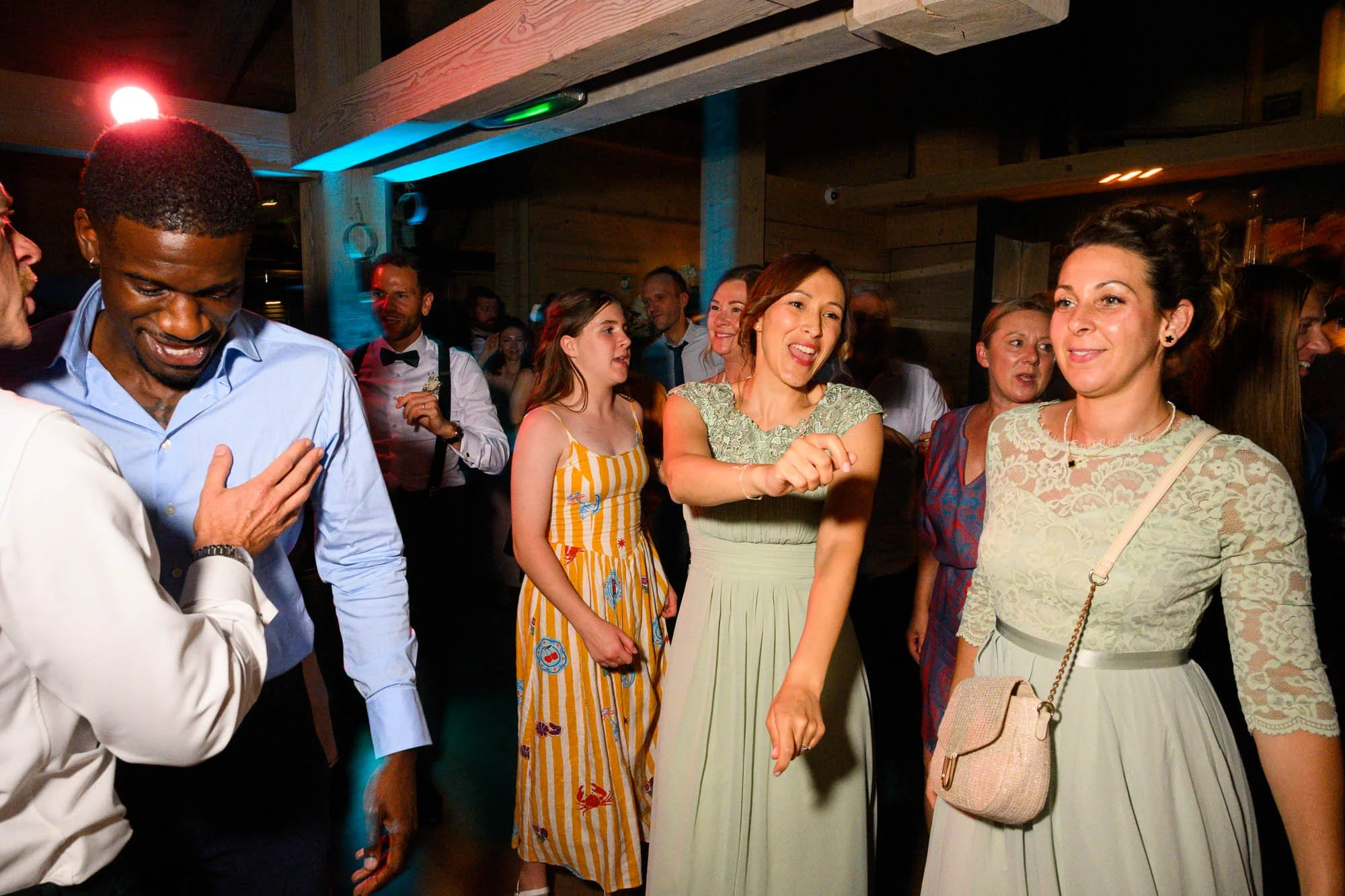 Groupe de personnes dansant et passant un bon moment lors d'une fête ou d'un événement social dans une ambiance chaleureuse avec éclairage coloré.