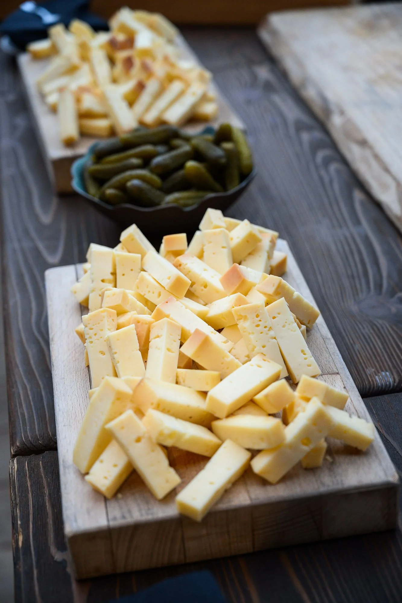 Plate de fromage coupé en morceaux, avec des cornichons et des frites en arrière-plan.