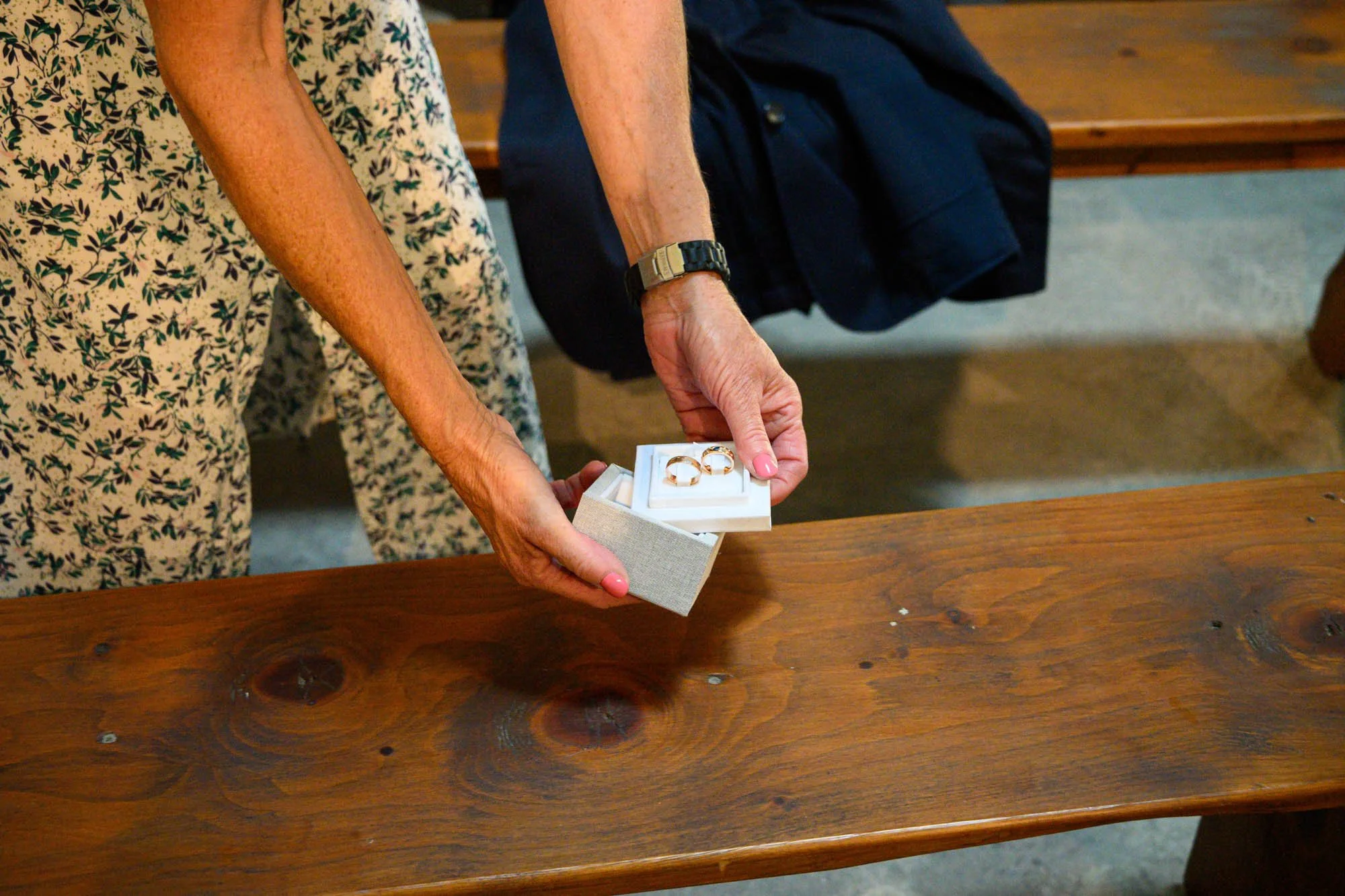 Une femme tendant une boîte contenant deux anneaux en or, probablement lors d'une cérémonie de mariage.