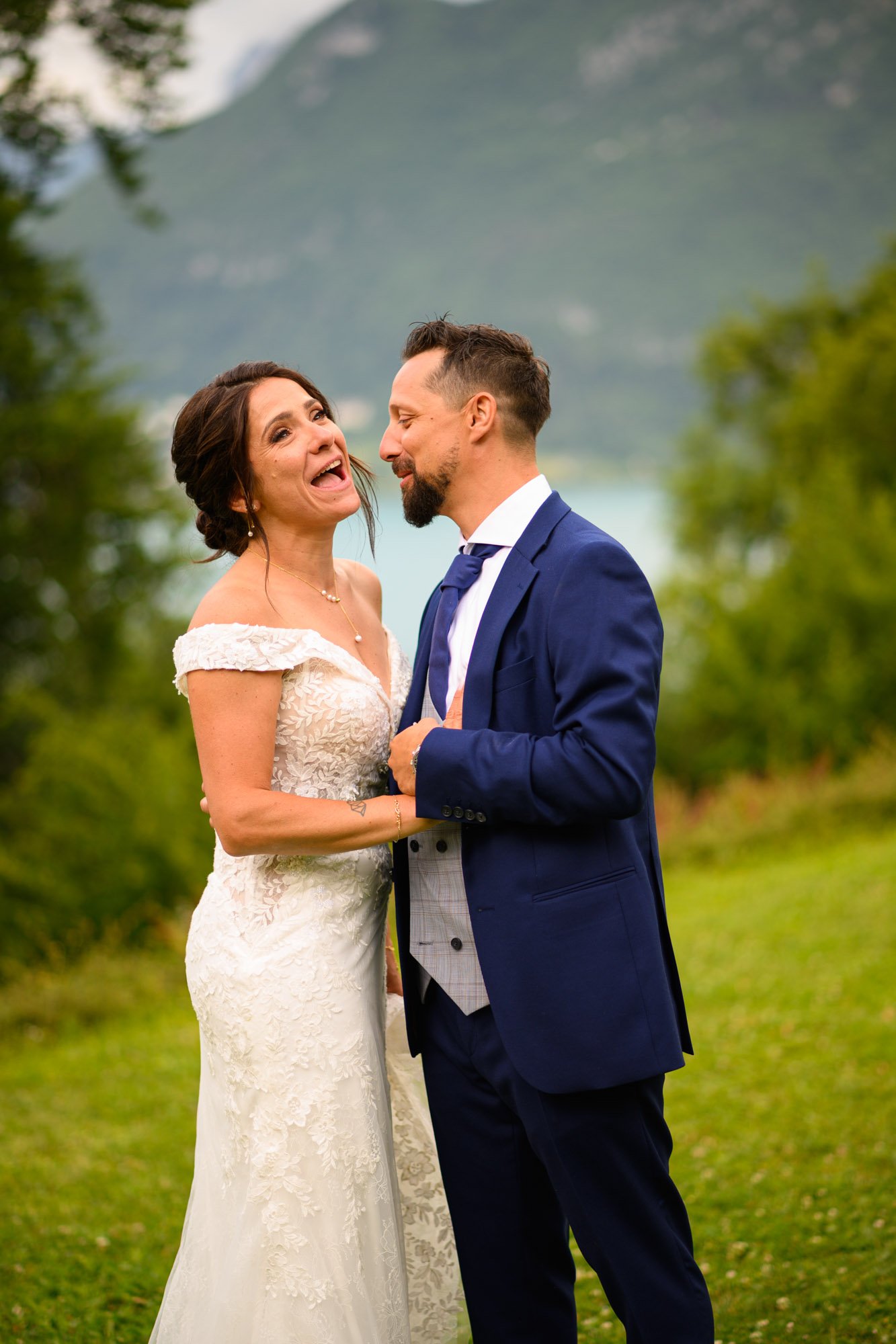 Un couple en mariage souriant et en train de s'amuser dans un extérieur avec des montagnes en arrière-plan.
