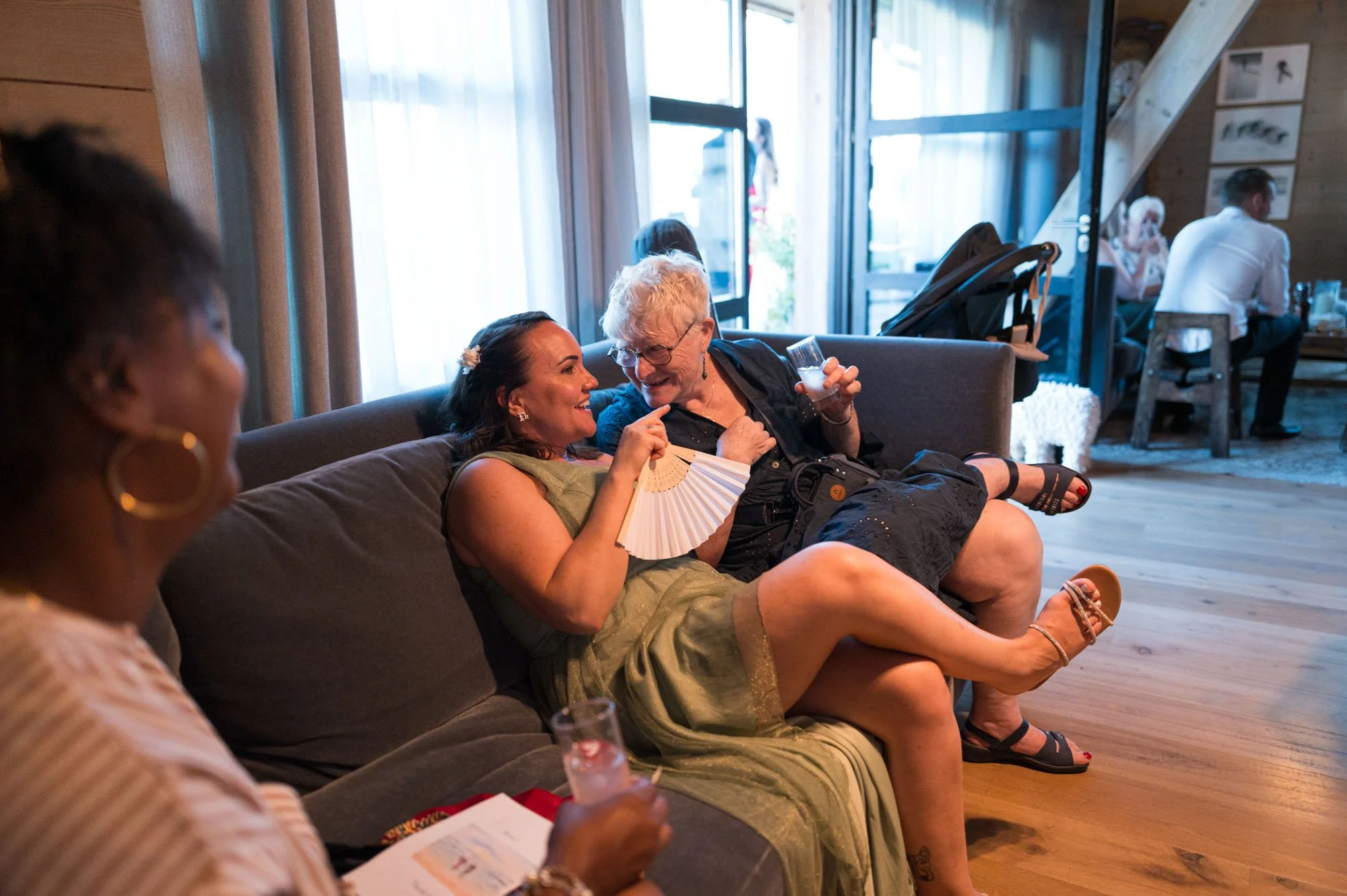 Deux femmes assises sur un canapé en train de discuter et de rire, lors d'une réunion ou d'une fête dans un intérieur chaleureux.