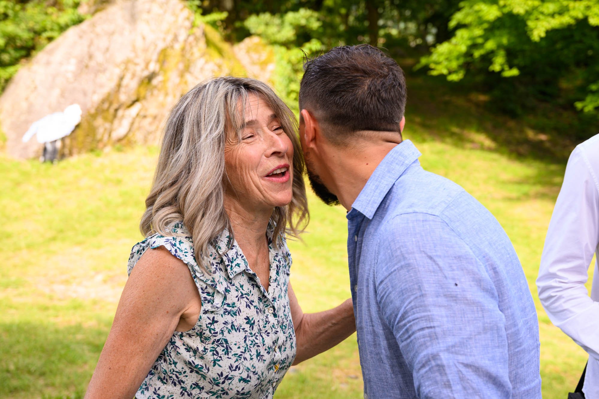 Deux personnes souriantes en train de parler dans un parc, silhouette d'un oiseau sur un rocher en arrière-plan, arbres verts.