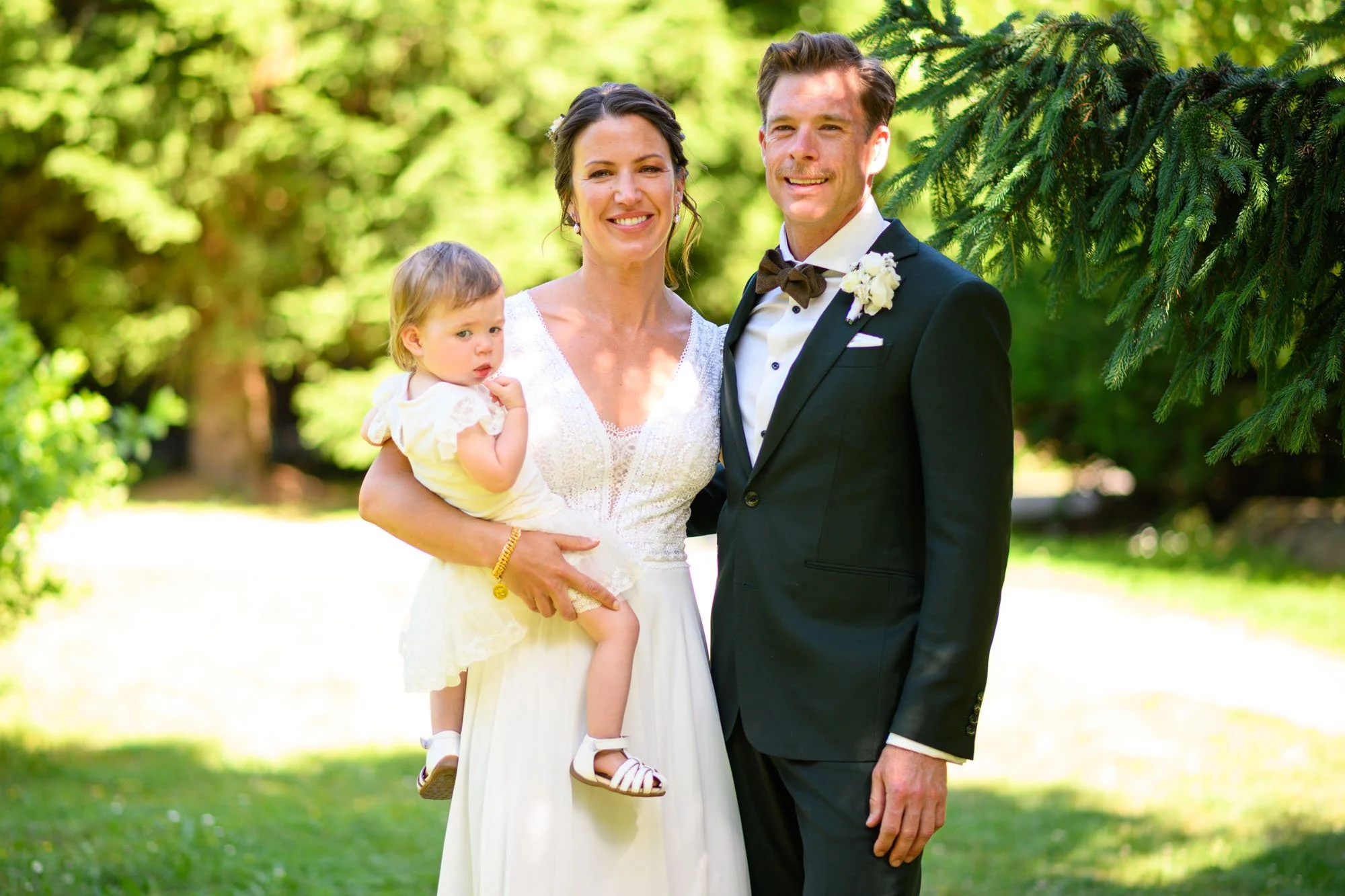 Un couple de mariés avec une jeune fille lors d'un mariage en plein air, dans un jardin verdoyant.