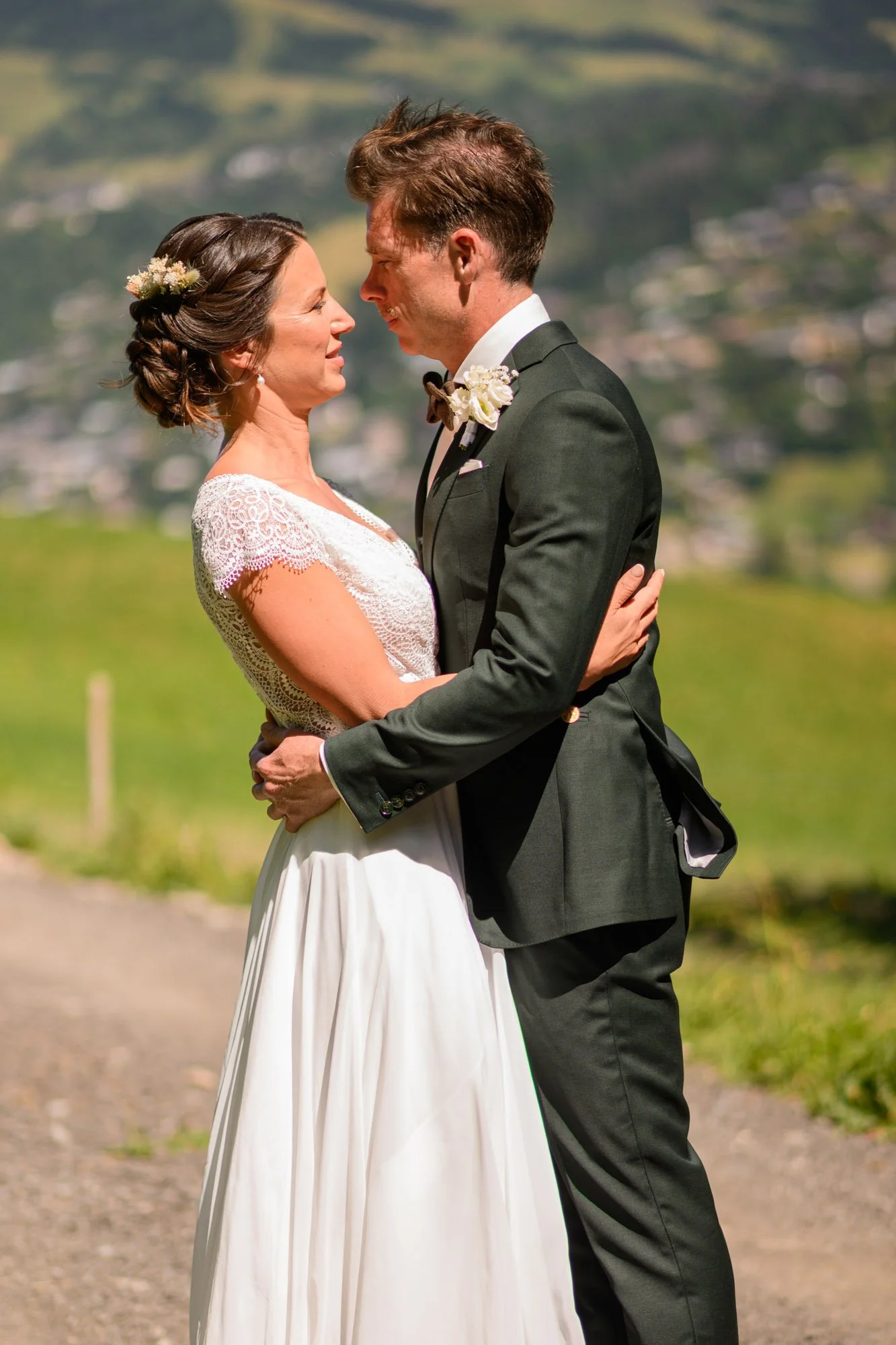 Un couple en habits de mariage se tenant face à face dans un paysage rural montagnard.