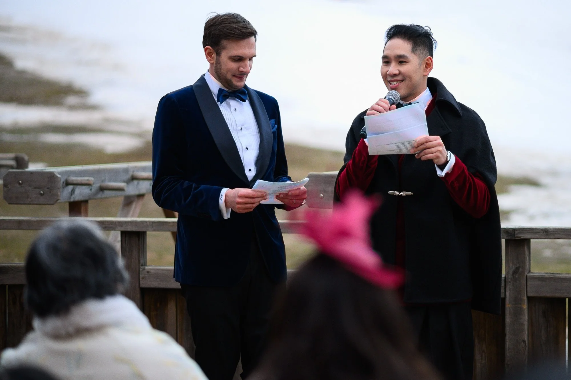 Deux hommes habillés en costume tiennent des discours lors d'une cérémonie en plein air avec un public devant eux.