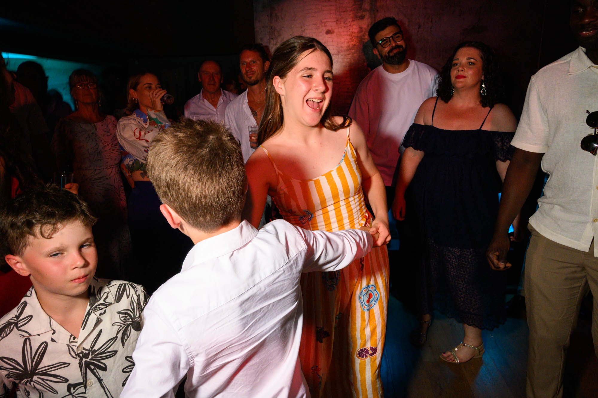 Groupe de personnes dansant lors d'une fête ou d'un événement social, en intérieur, avec ambiance chaleureuse et décontractée.