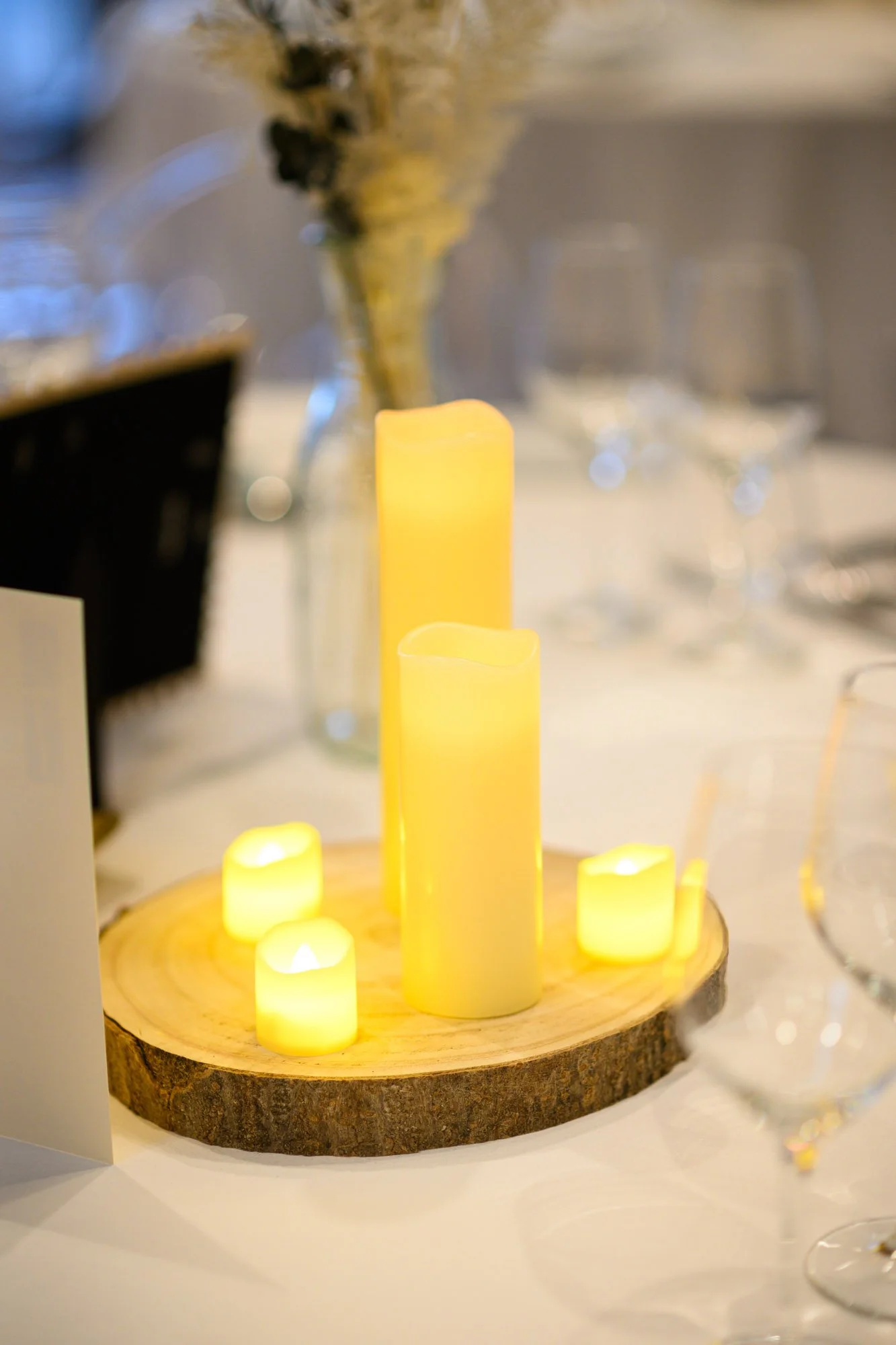 Bougeoir décoratif avec des bougies LED de différentes tailles sur une planche en bois, dans un cadre de table de dîner.