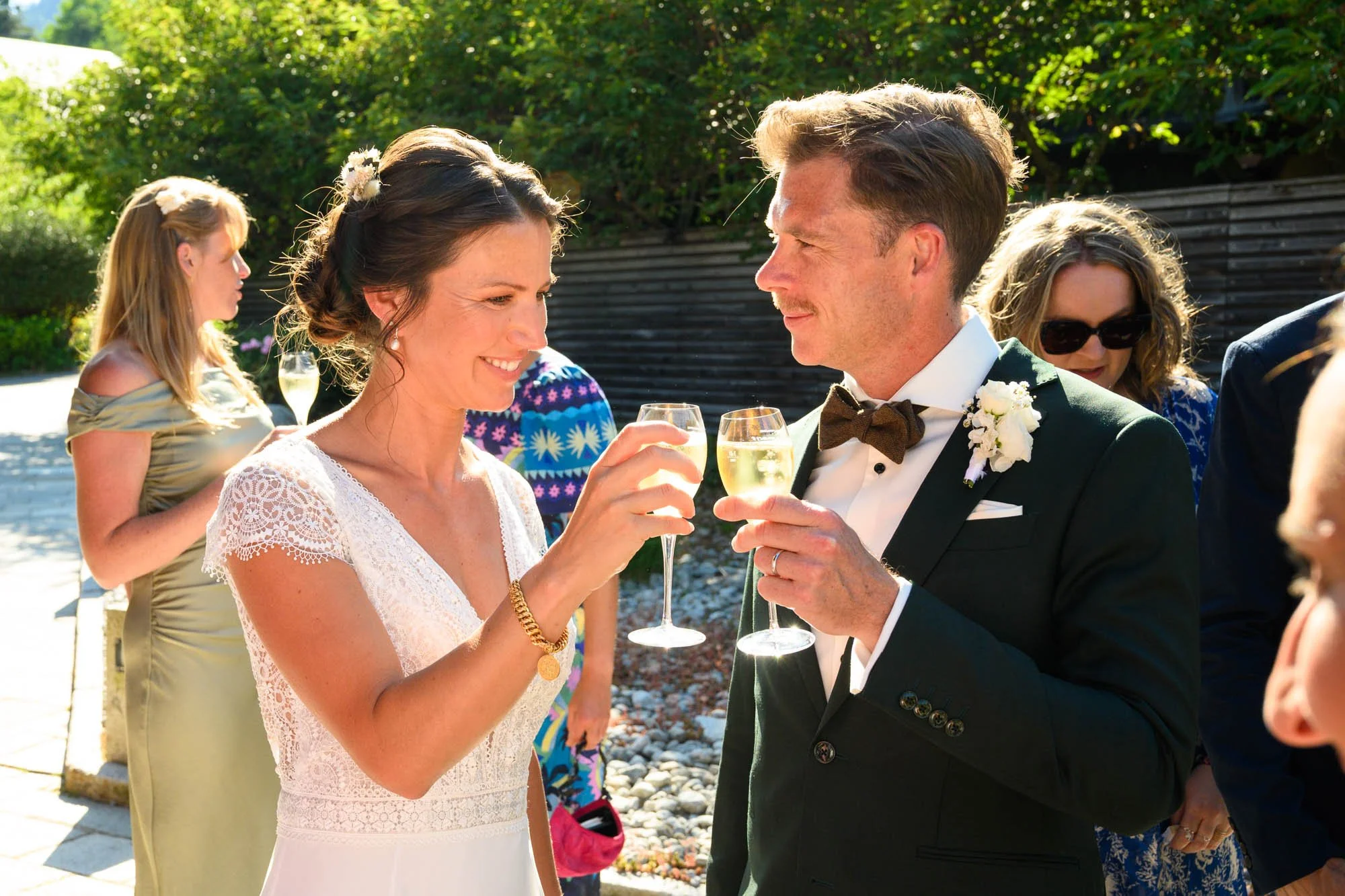 Un couple de mariés trinque lors de leur mariage en extérieur, entourés d'invités.