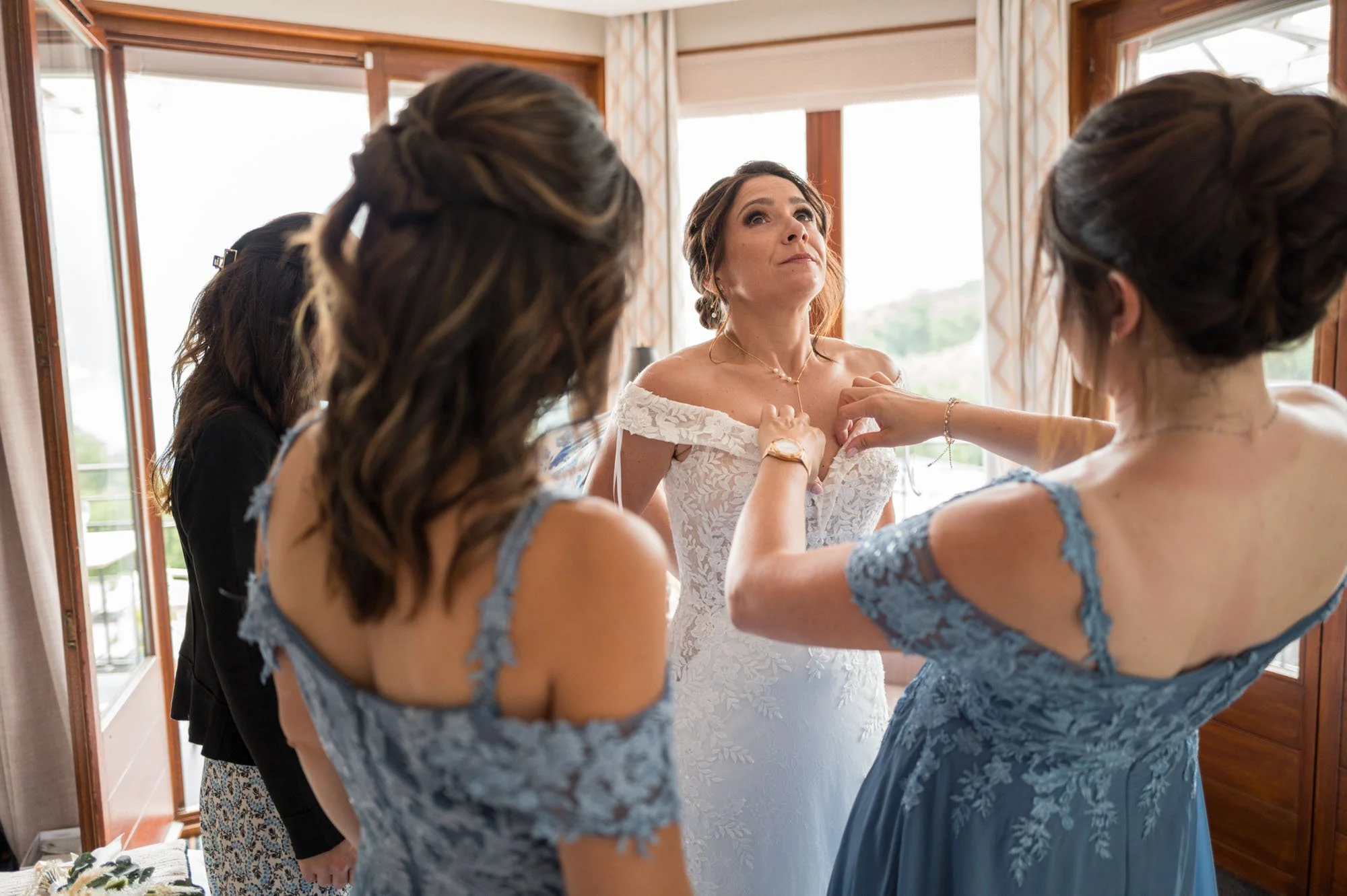Femme en robe de mariée blanche entourée de femmes en robes bleues lors de la préparation au mariage.