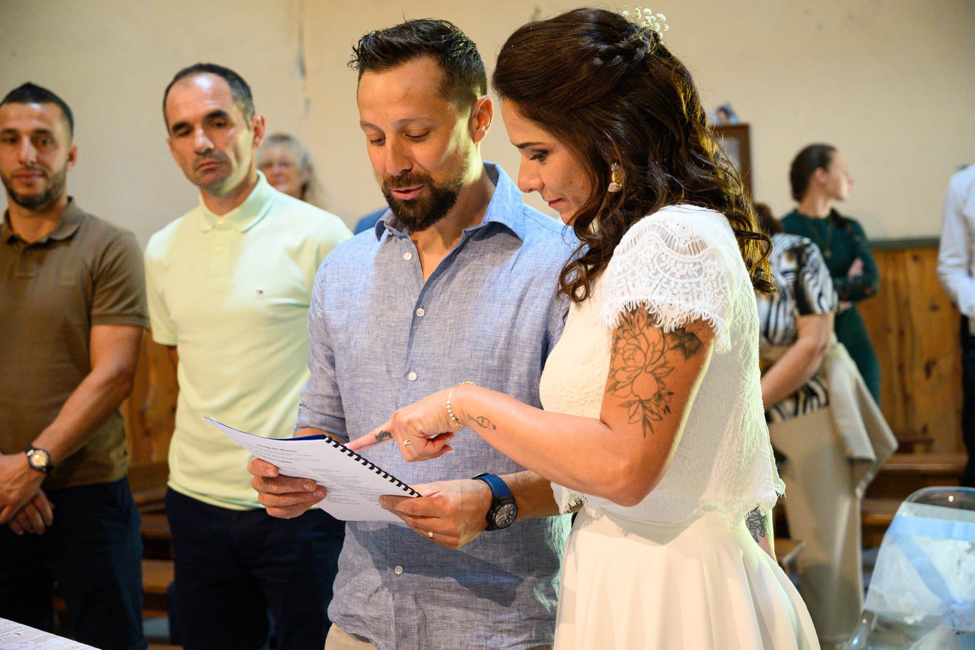 Un couple échange leurs vœux de mariage dans une église, entouré d'autres personnes.