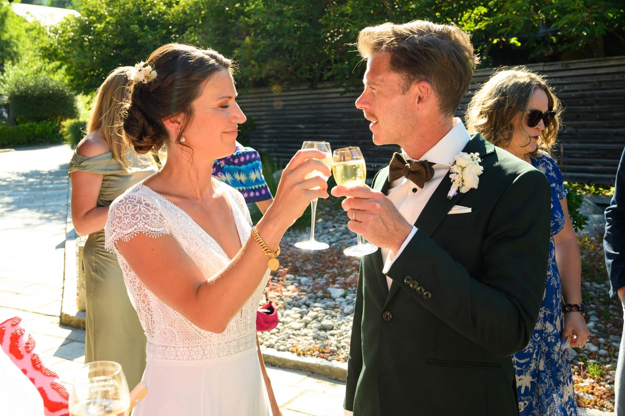 Un couple en tenue de mariage célébrant avec des flûtes à champagne lors d'une cérémonie en extérieur ensoleillée.