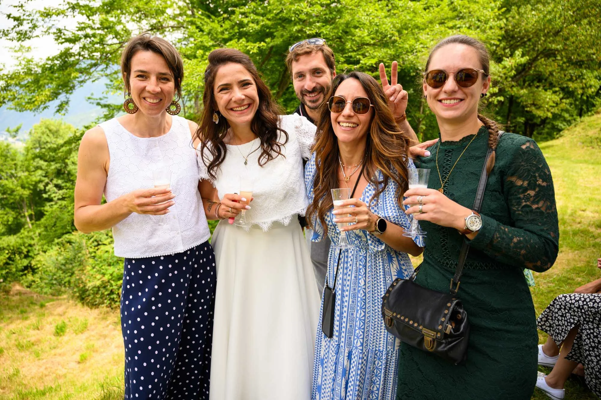 Groupe de cinq personnes souriantes lors d'une fête en plein air, tenant des verres, dans un environnement verdoyant.