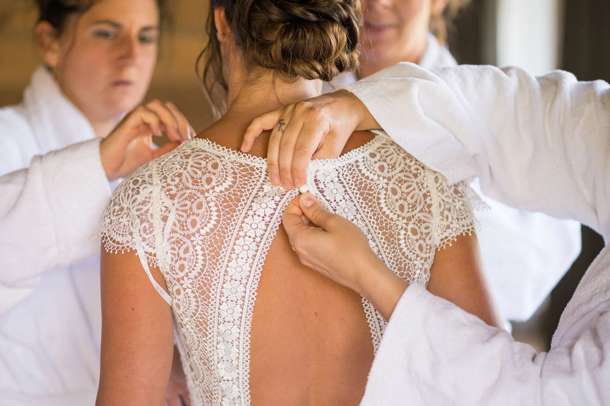 Des femmes en blanc aident une femme à se faire habiller en blanc pour une occasion spéciale, probablement un mariage.