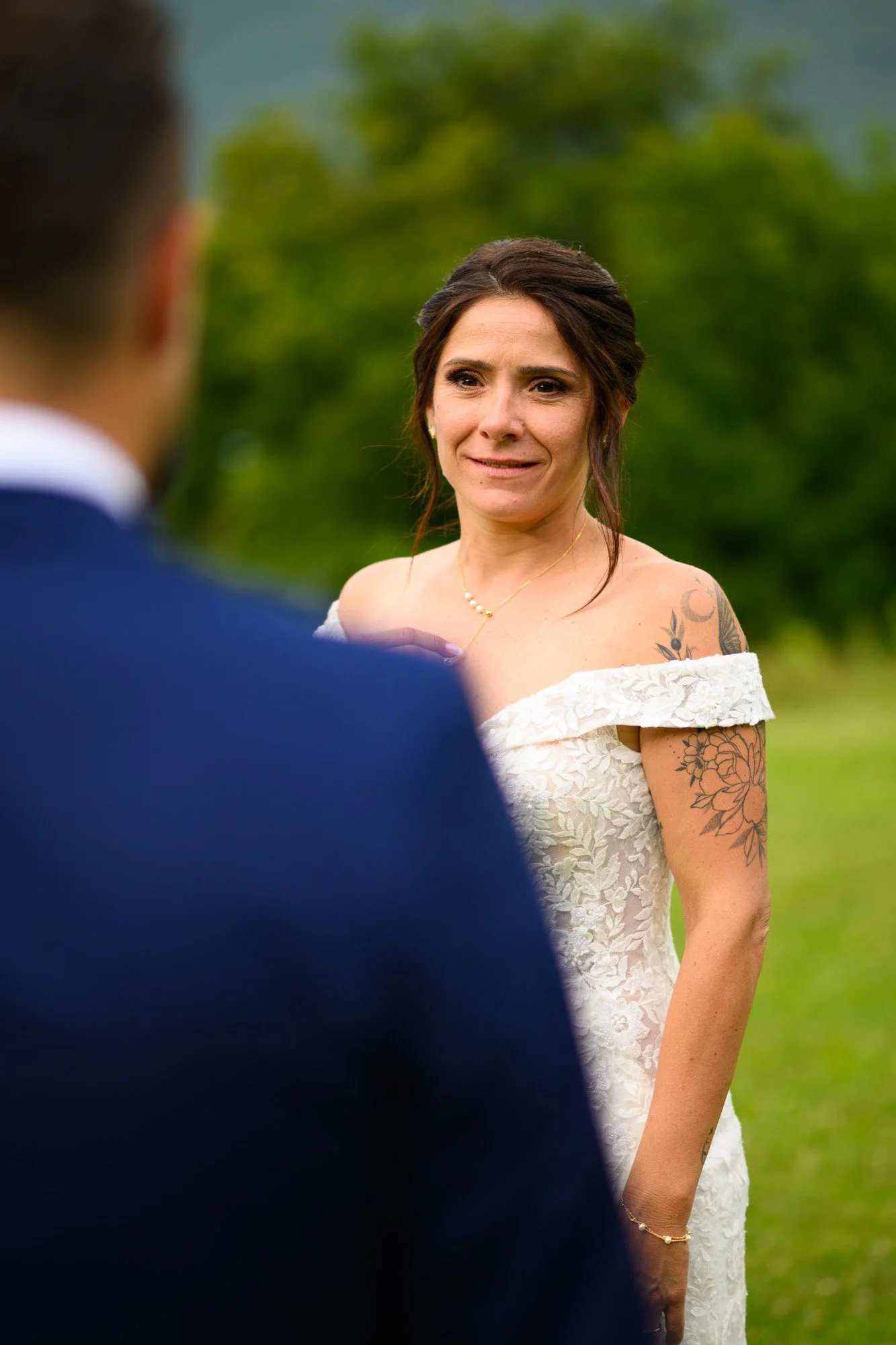 Une femme en robe de mariage regarde un homme lors d'une cérémonie en extérieur, avec des arbres en arrière-plan.