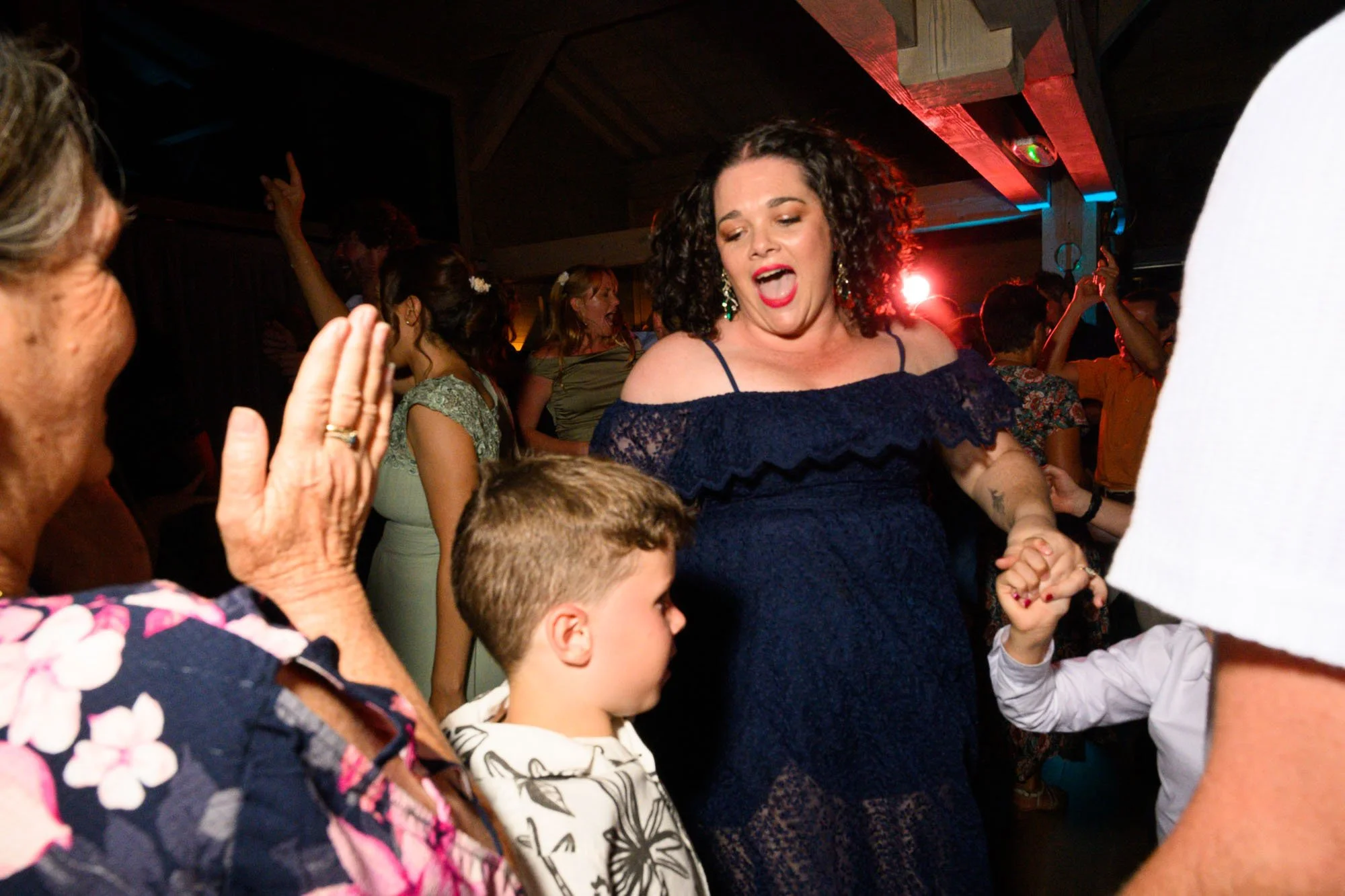 Des personnes dansant et souriant lors d'une fête en intérieur, ambiance festive avec lumières colorées.