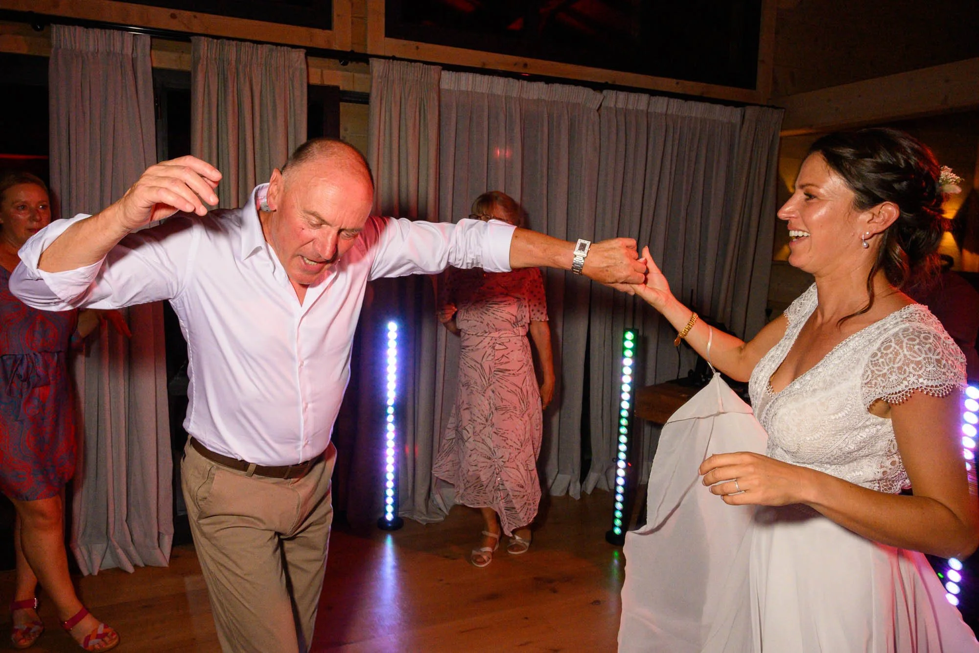 Un homme en chemise blanche et une femme en robe de mariage dansant ensemble lors d'une fête.