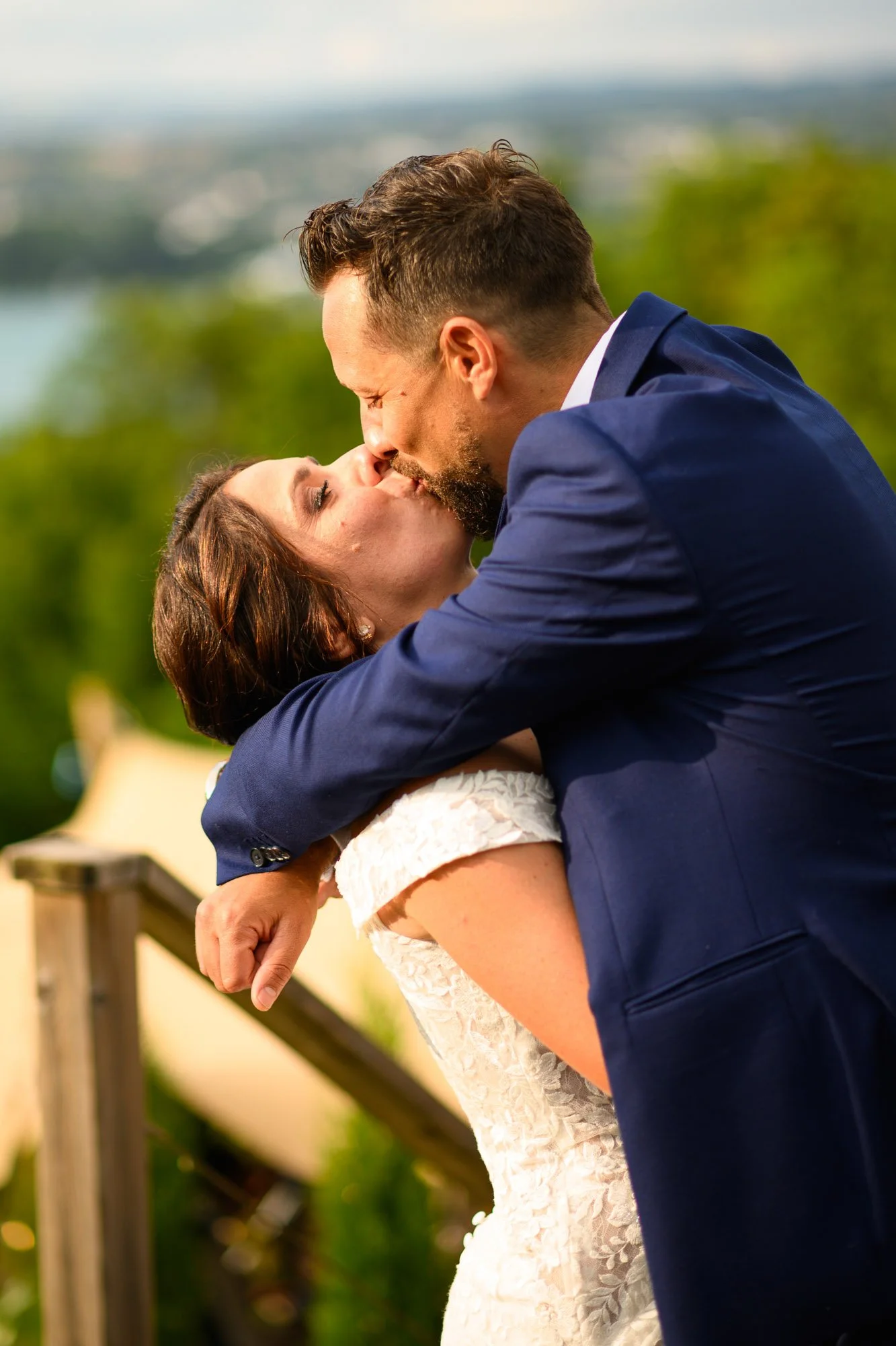 Un couple en costume s'embrassant lors d'une cérémonie en plein air, avec un fond flou de nature et un lac.