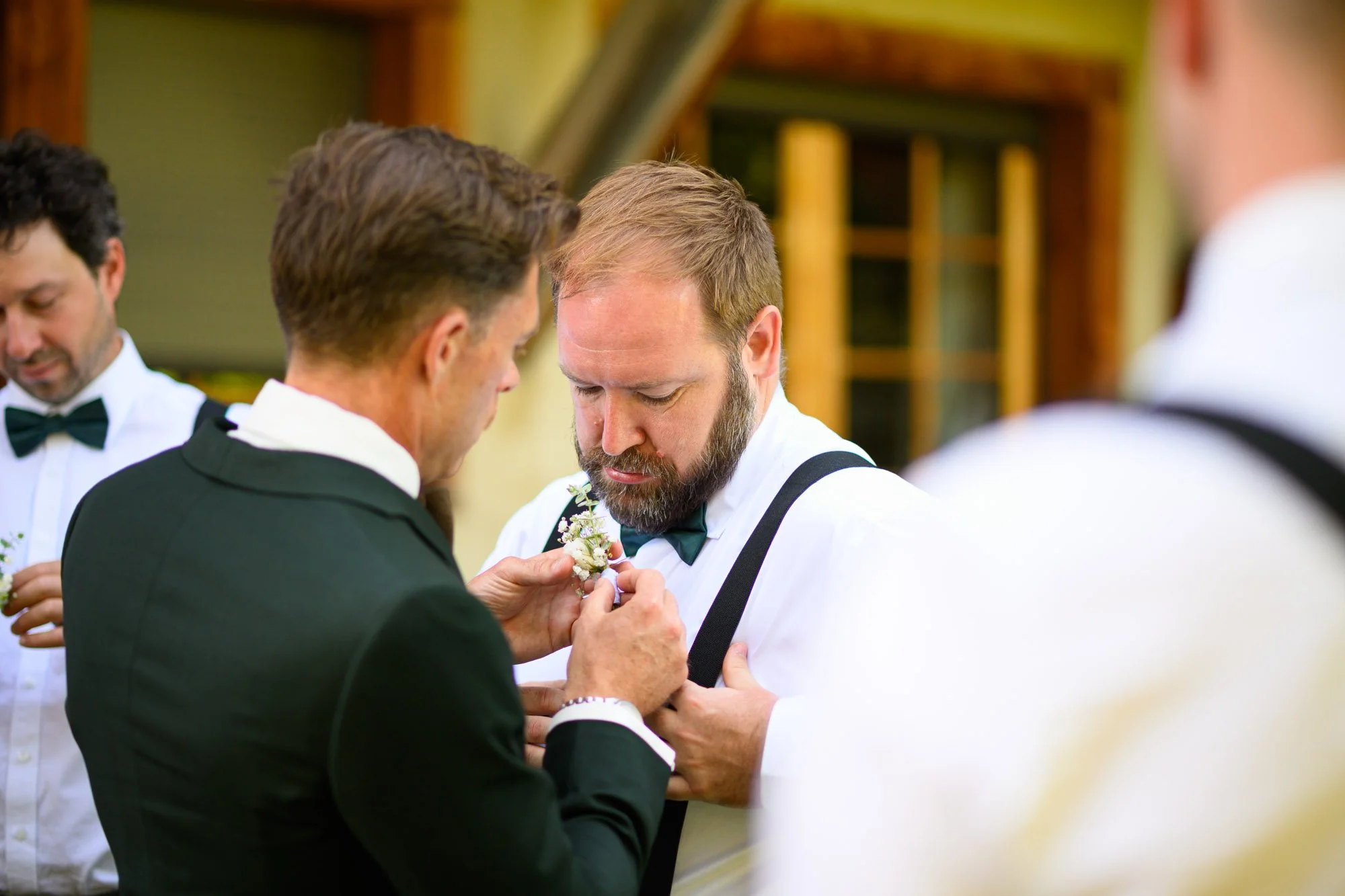 Homme en costume noir recevant une boutonnière d'un autre homme lors d'une cérémonie de mariage.