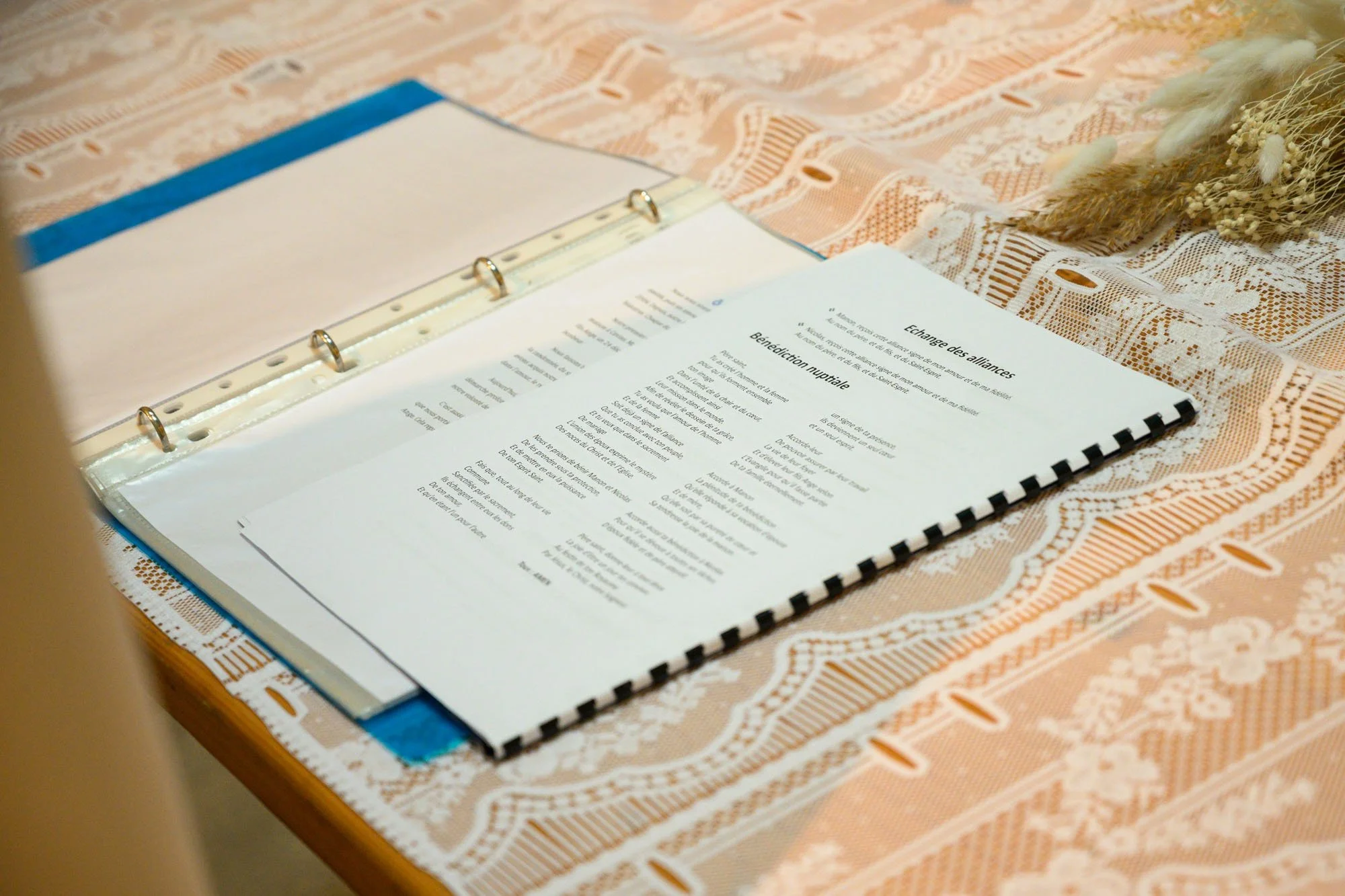 Un livre ou un carnet ouvert avec des pages de texte en français, posé sur une nappe en tissu à motif blanc et orange, à côté de quelques fleurs séchées.