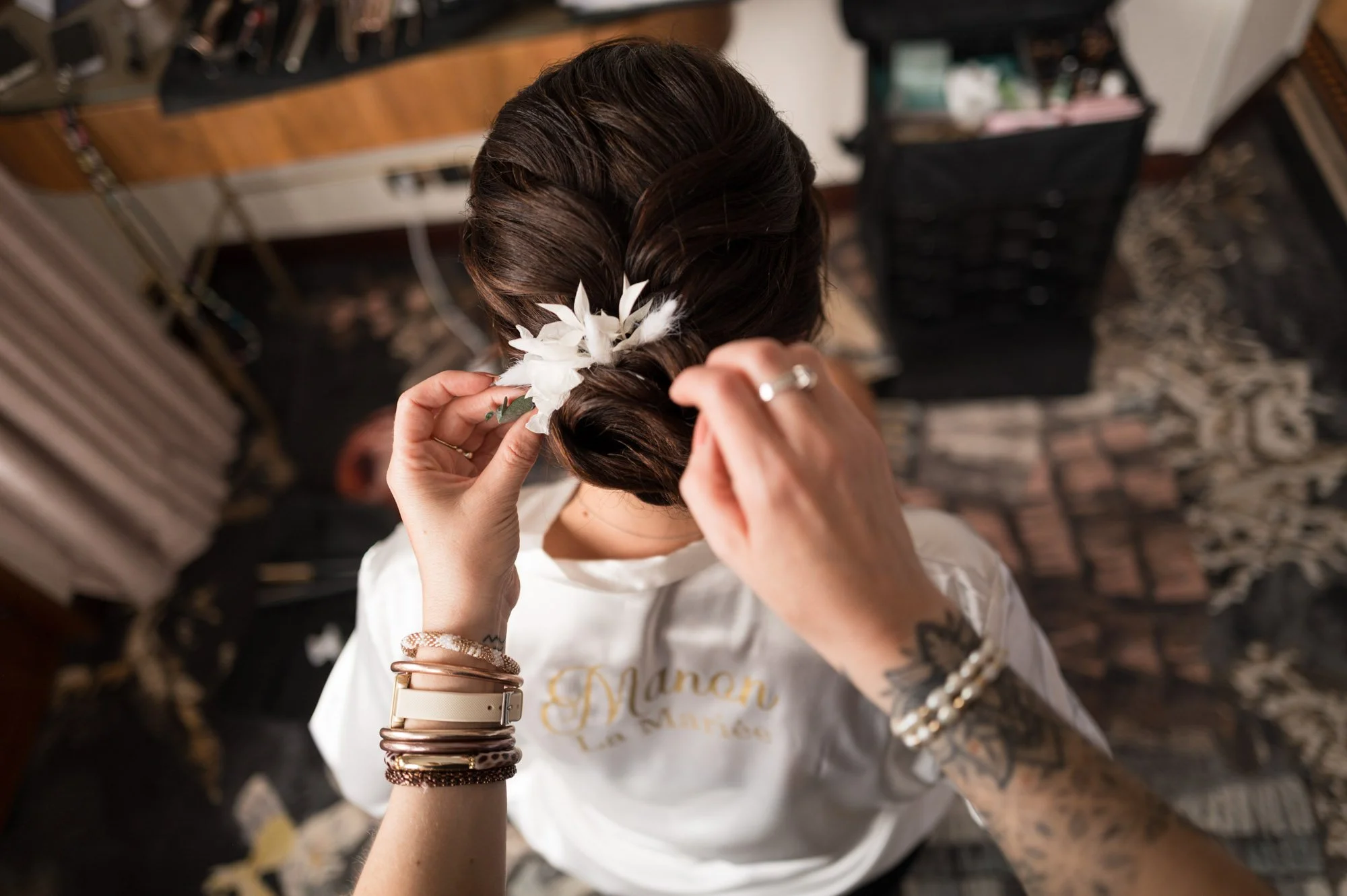 Femme préparant une coiffure avec des fleurs blanches, vue du dessus, dans un espace intérieur avec un tapis et des meubles.