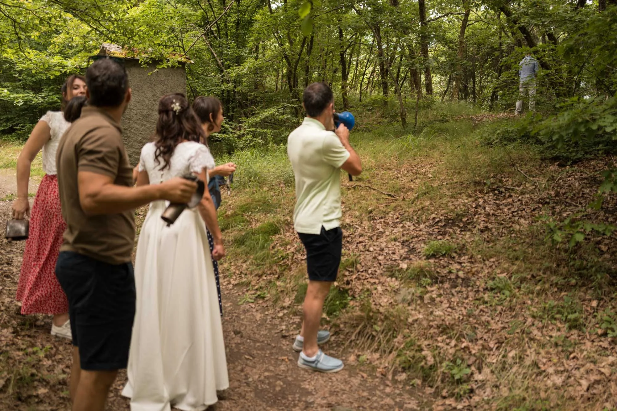 Groupe de personnes dans une forêt, avec une femme en robe blanche, en train d'observer quelque chose dans la végétation.