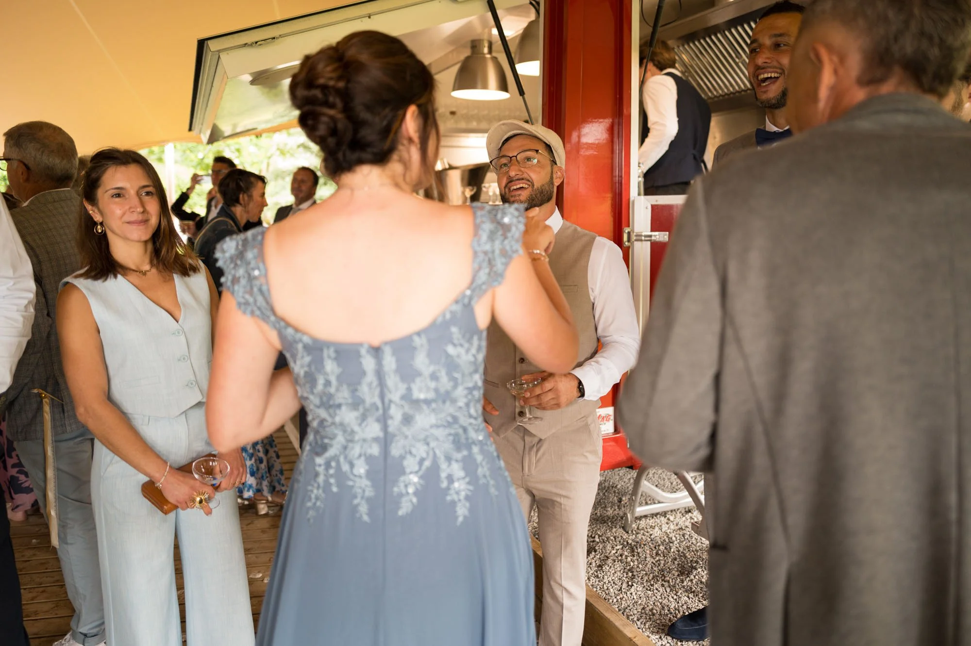Un groupe de personnes habillées élégamment en train de converser lors d'un événement ou d'une fête. On peut voir une femme avec une robe bleu ciel à dentelle, d'autres personnes souriantes autour, dans un cadre intérieur avec une ambiance festive.