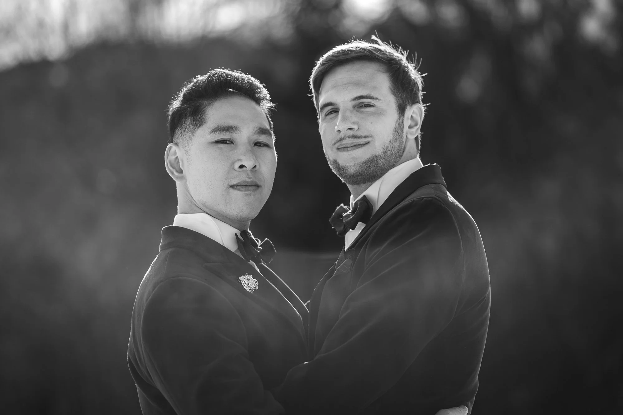 Deux hommes habillés en smoking tiennent la main, regardent l'objectif, en arrière-plan un paysage flou.