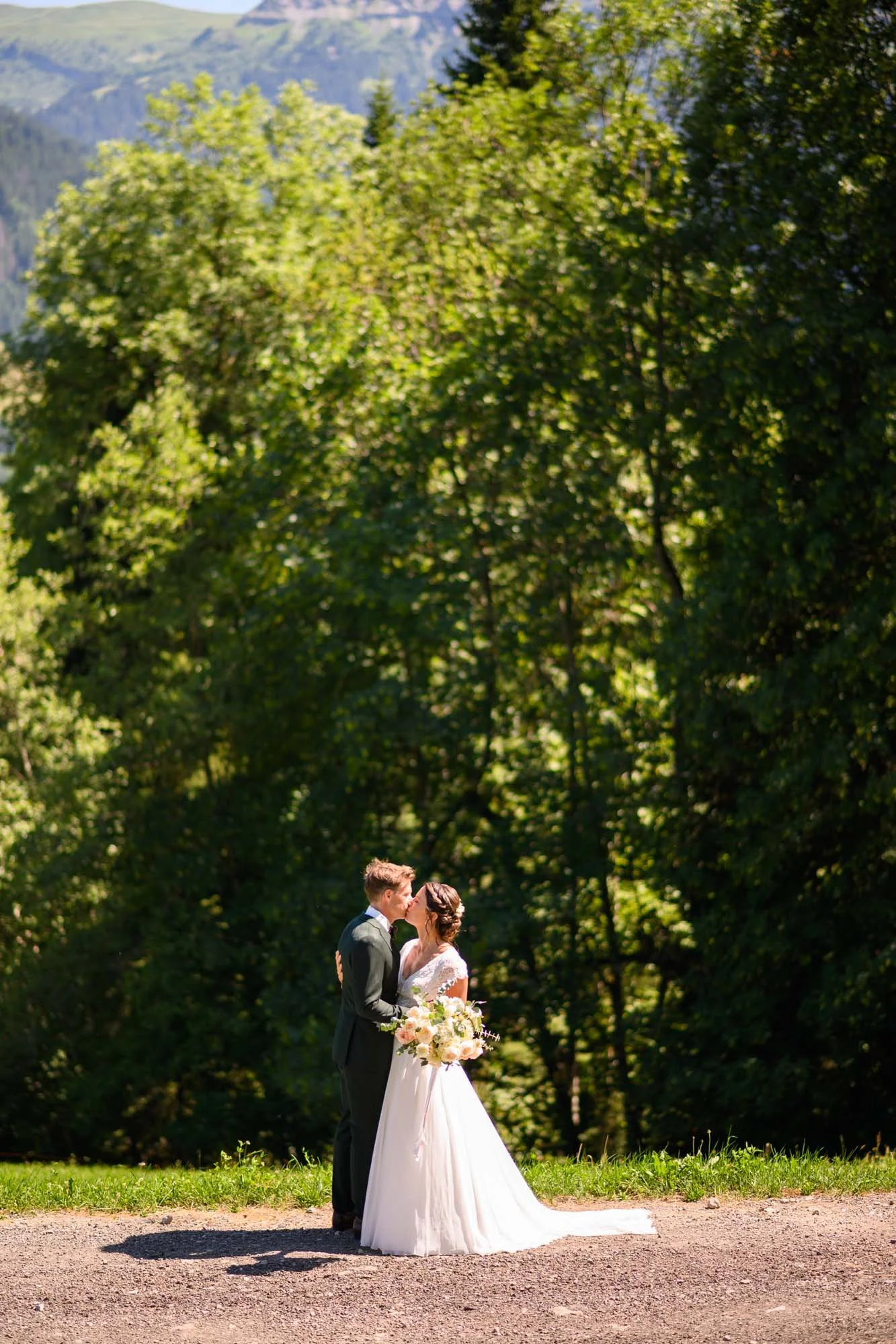 Un couple de mariés en robe et costume, s'embrassant dans un parc verdoyant, lors d'un mariage en plein air
