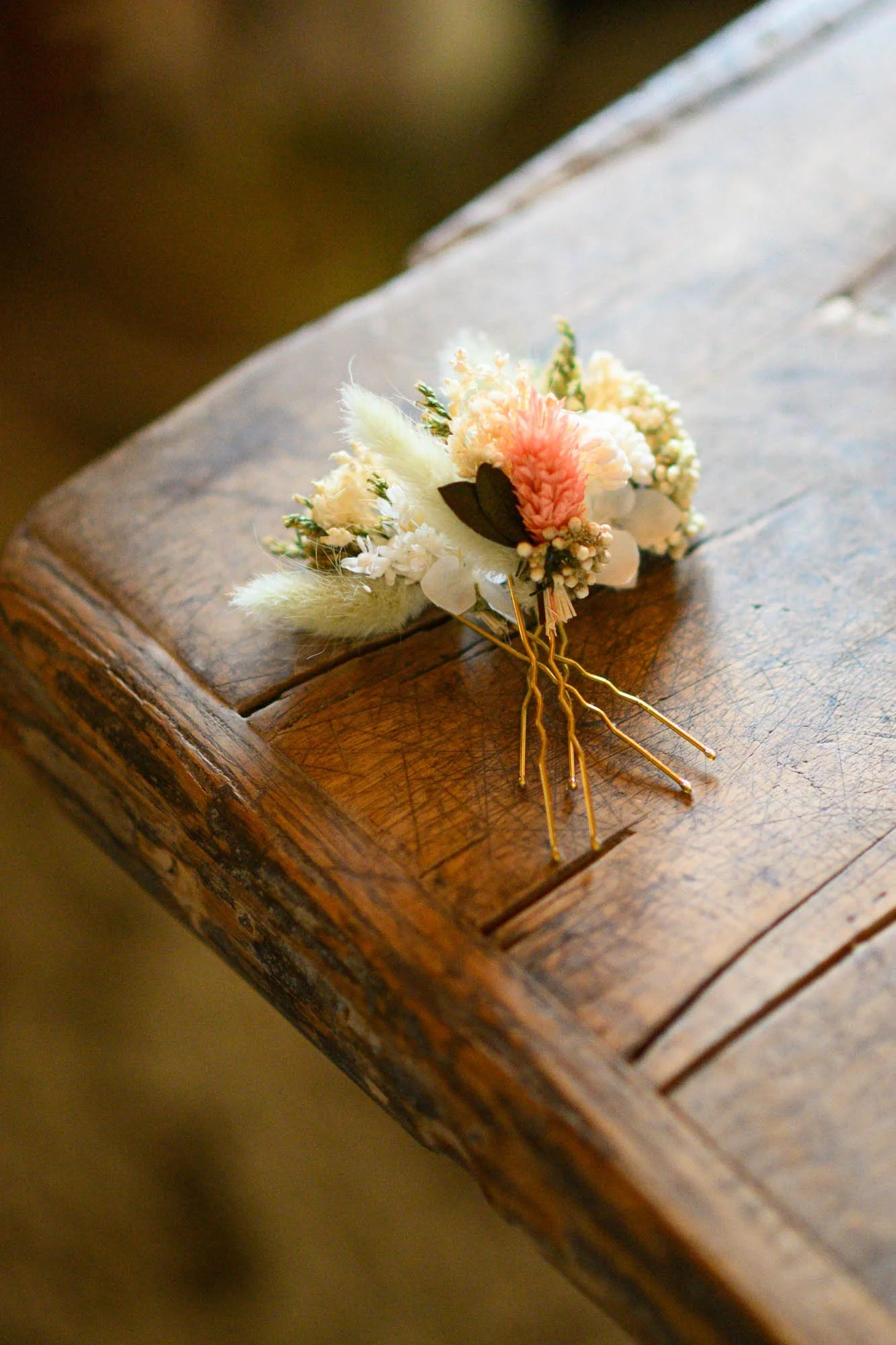 Un bouton de mariée en fleurs blanches, roses et vertes posé sur une table en bois.