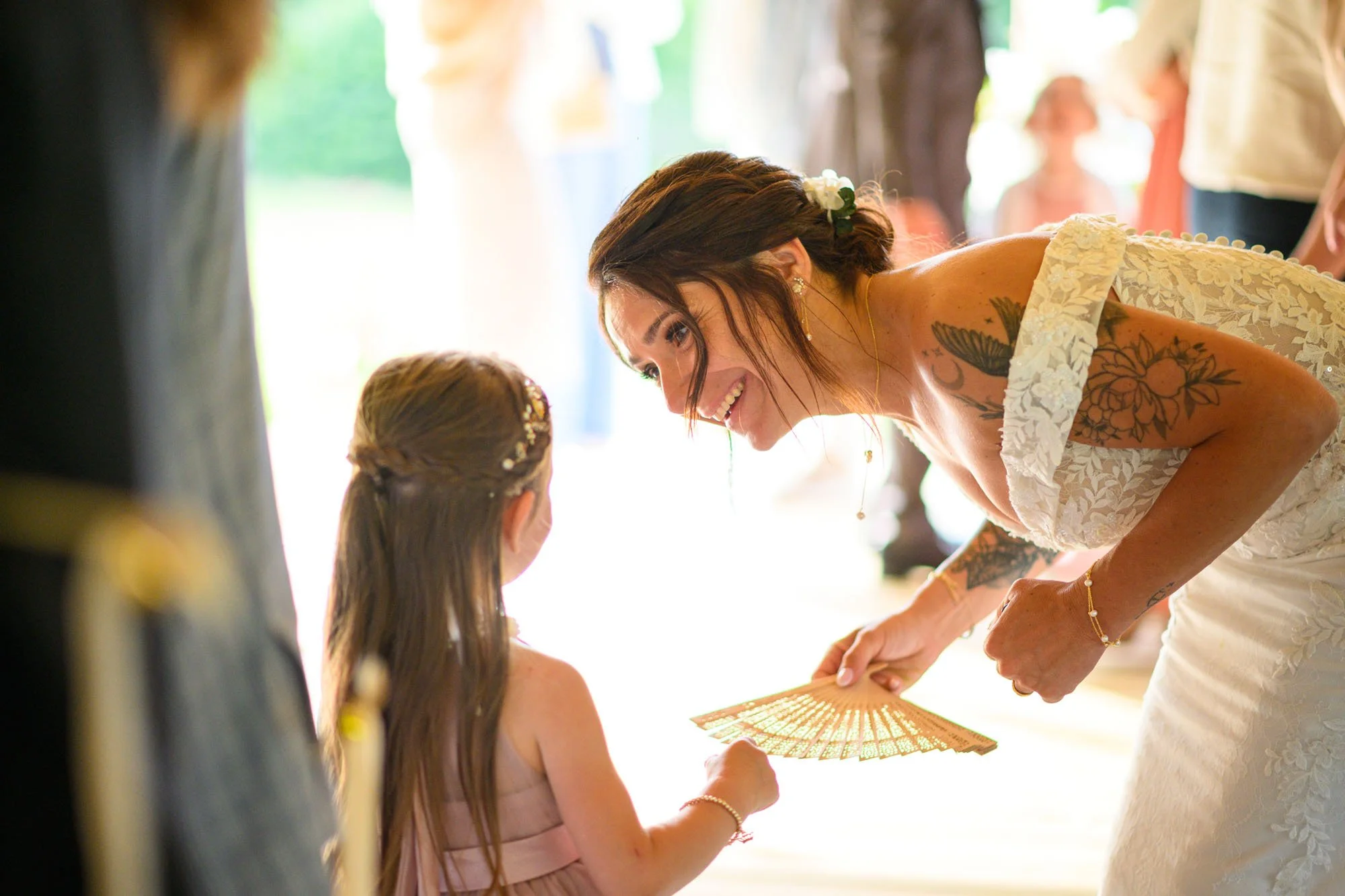 Une femme en robe de mariée souriante tend un objet à une petite fille lors d'une cérémonie de mariage