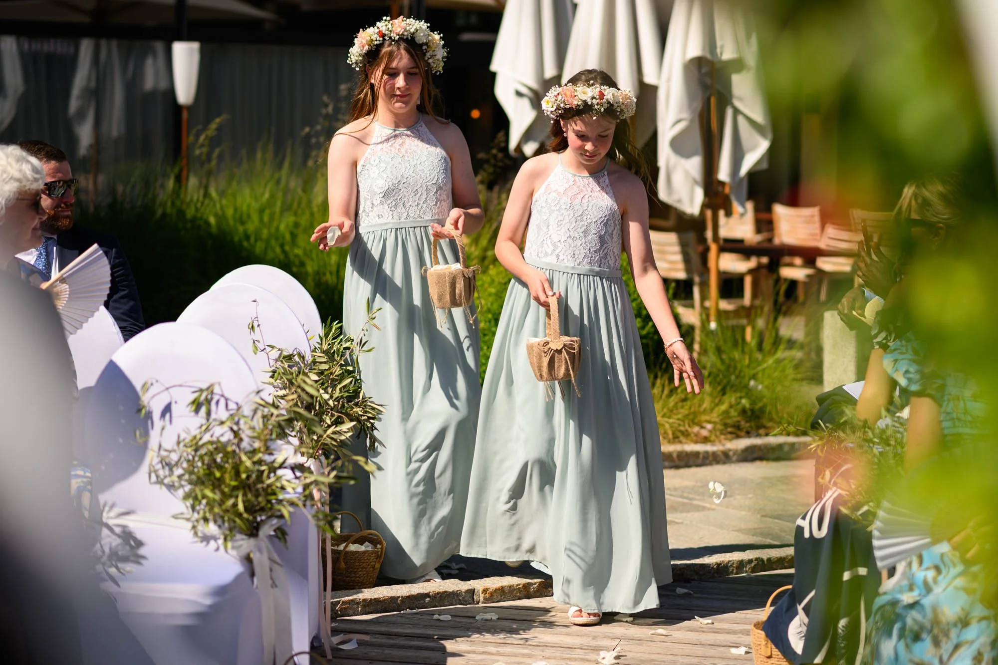 Deux jeunes filles portant des robes longues vert clair avec des couronnes de fleurs participent à une cérémonie en plein air.