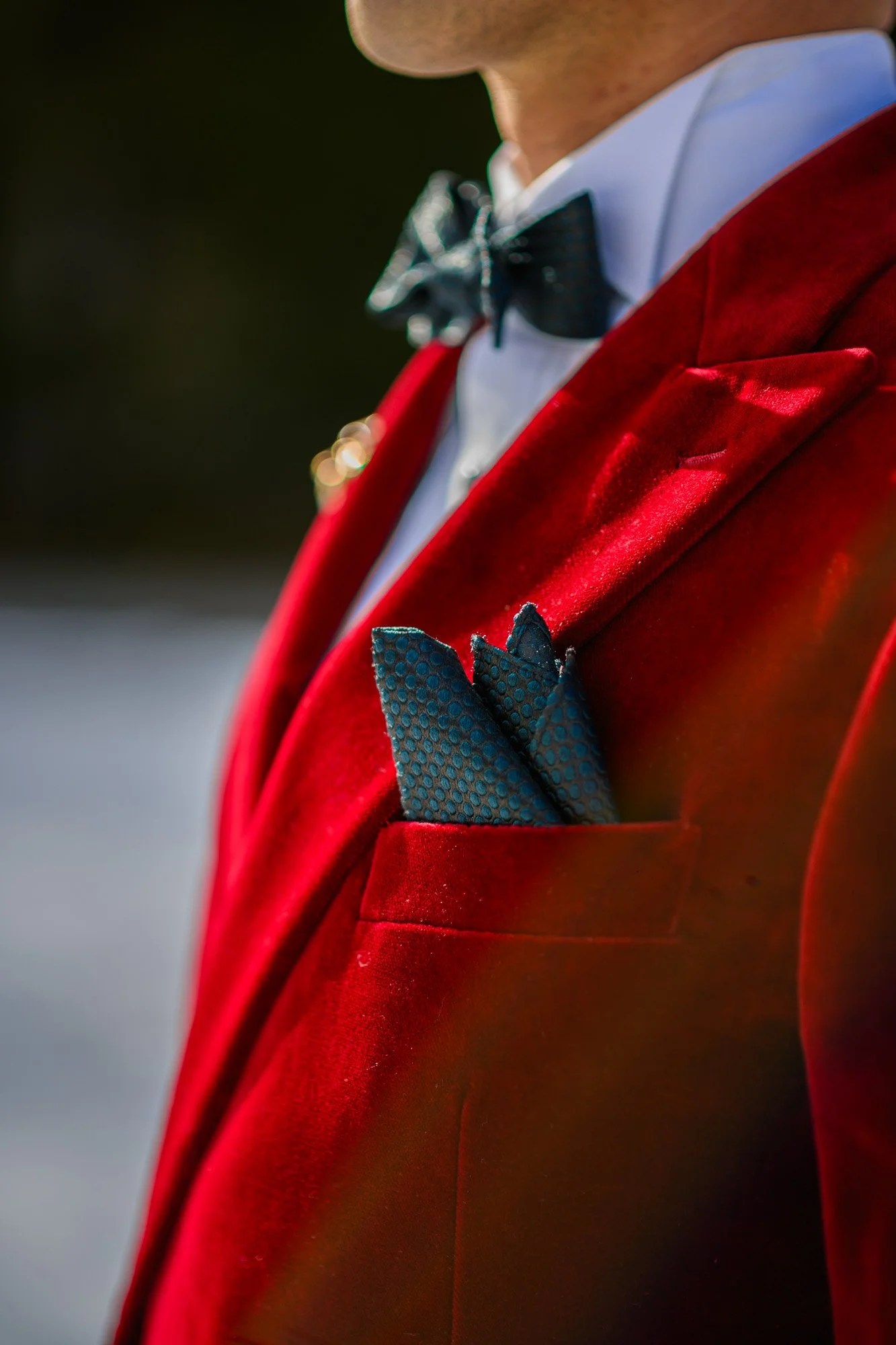 Homme portant un costume rouge en velours, chemise blanche, nœud papillon noir et pochette coordonnée dans la poche de la veste.