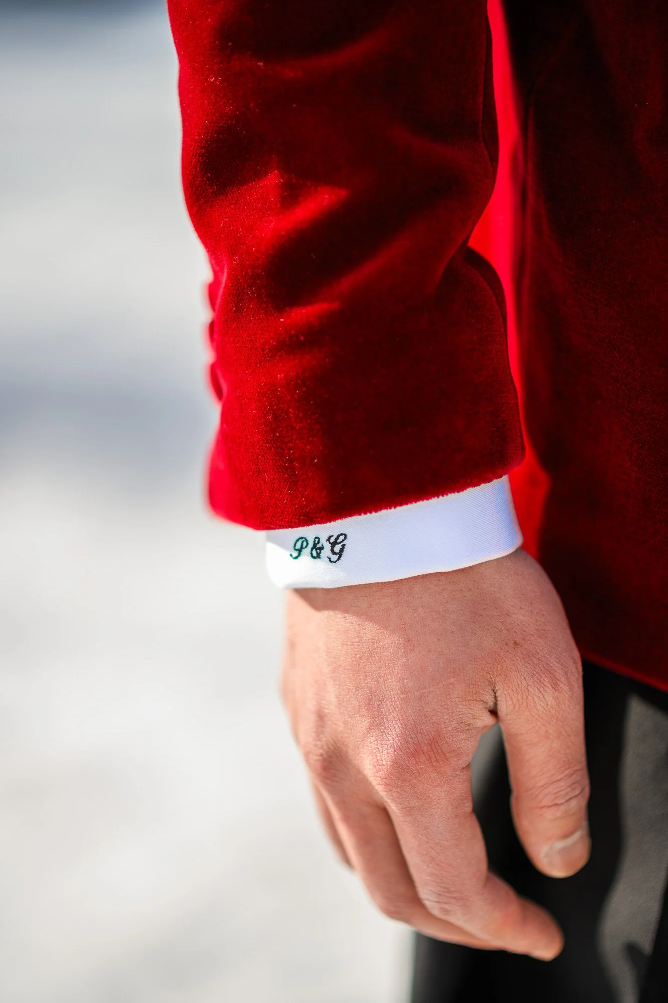 Zoom sur un poignet portant une manche de vêtement rouge, avec un bout blanc avec les initiales P&G en noir, et une main qui tient un objet noir.