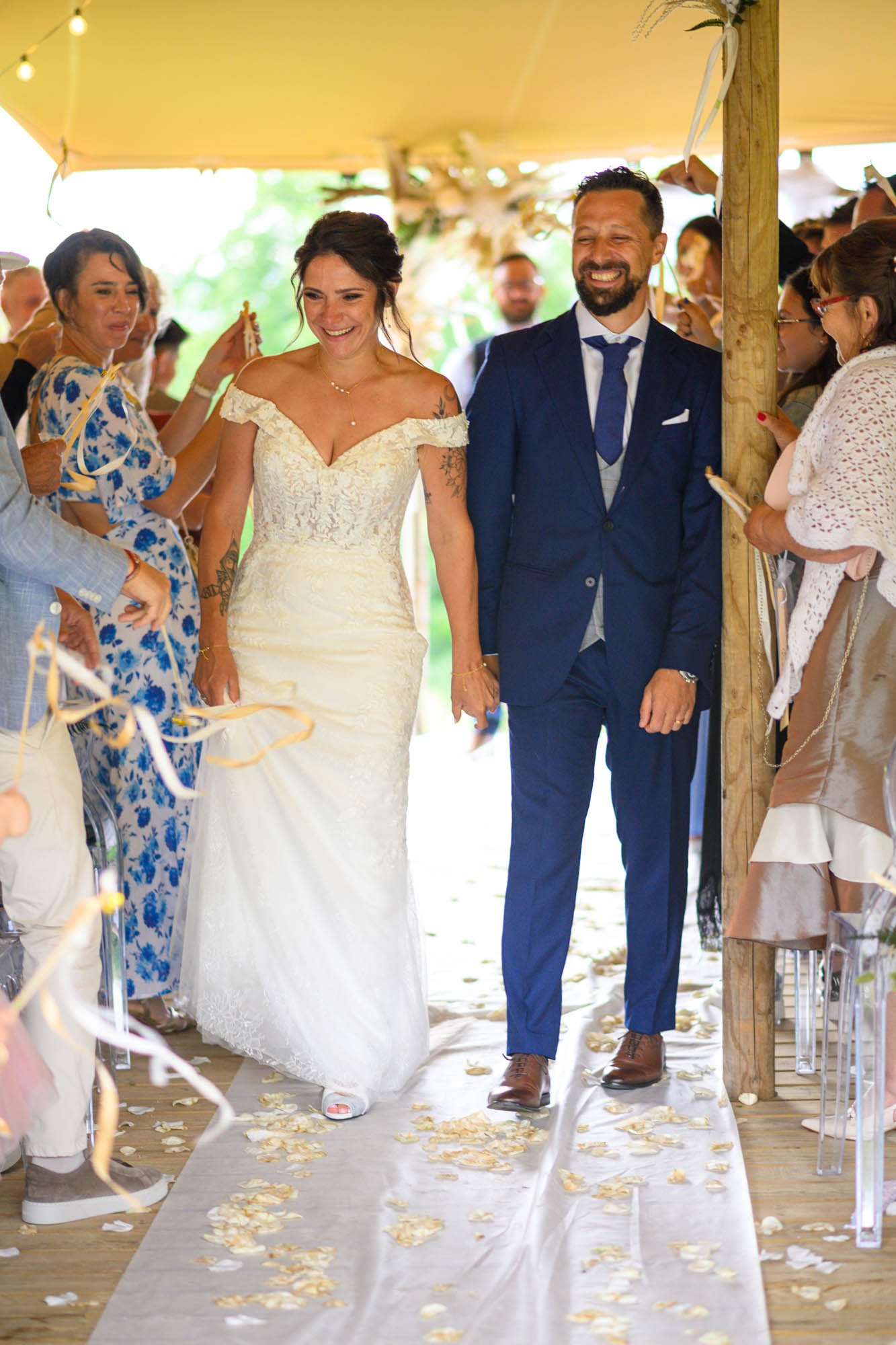 Un couple de mariés marche dans une allée décorée lors de leur mariage, entourés d'invités.