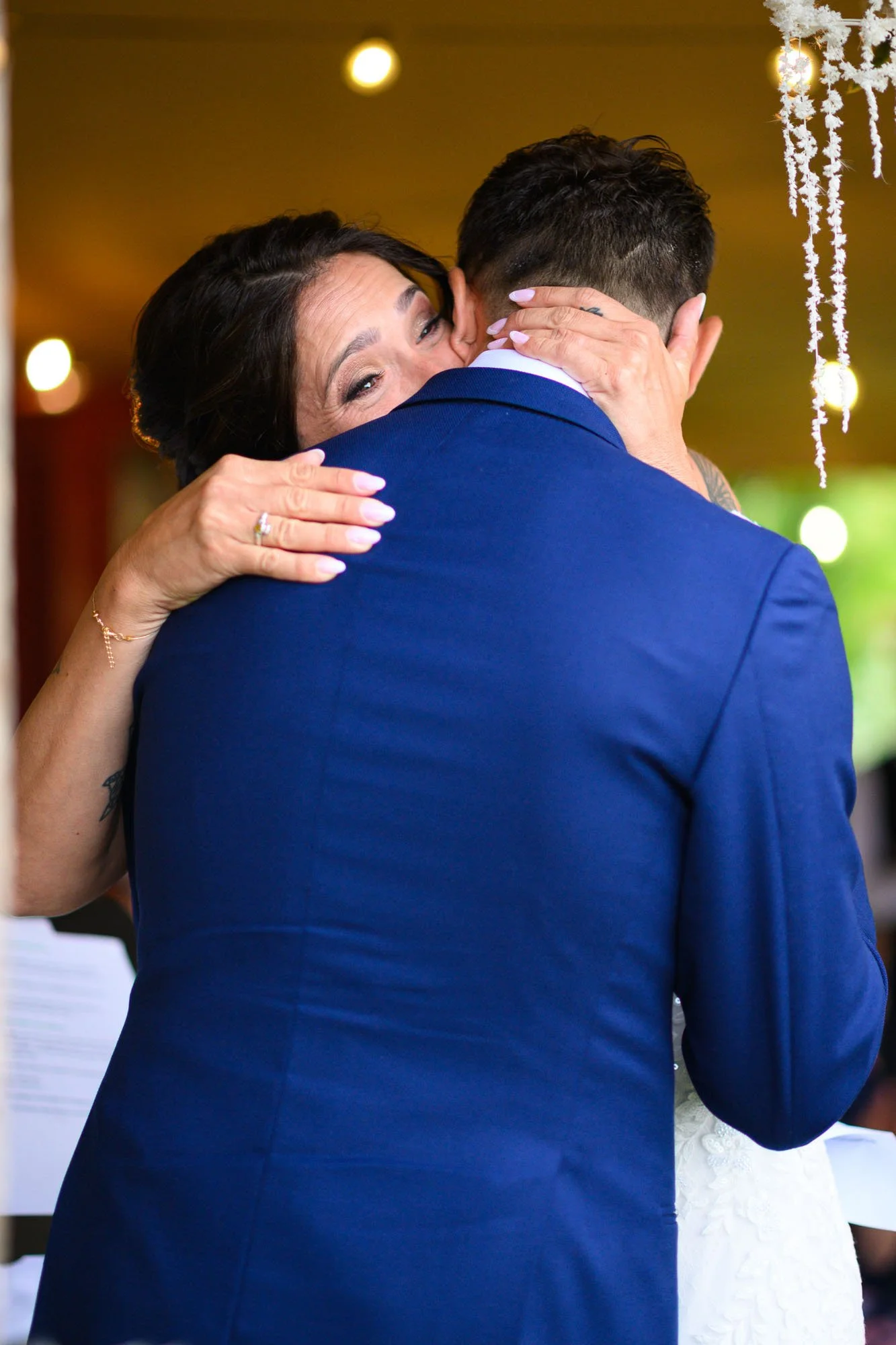 Une femme et un homme en costume s'embrassent lors d'une occasion spéciale, probablement un mariage, dans un décor festif avec des décorations suspendues blanc et des lumières