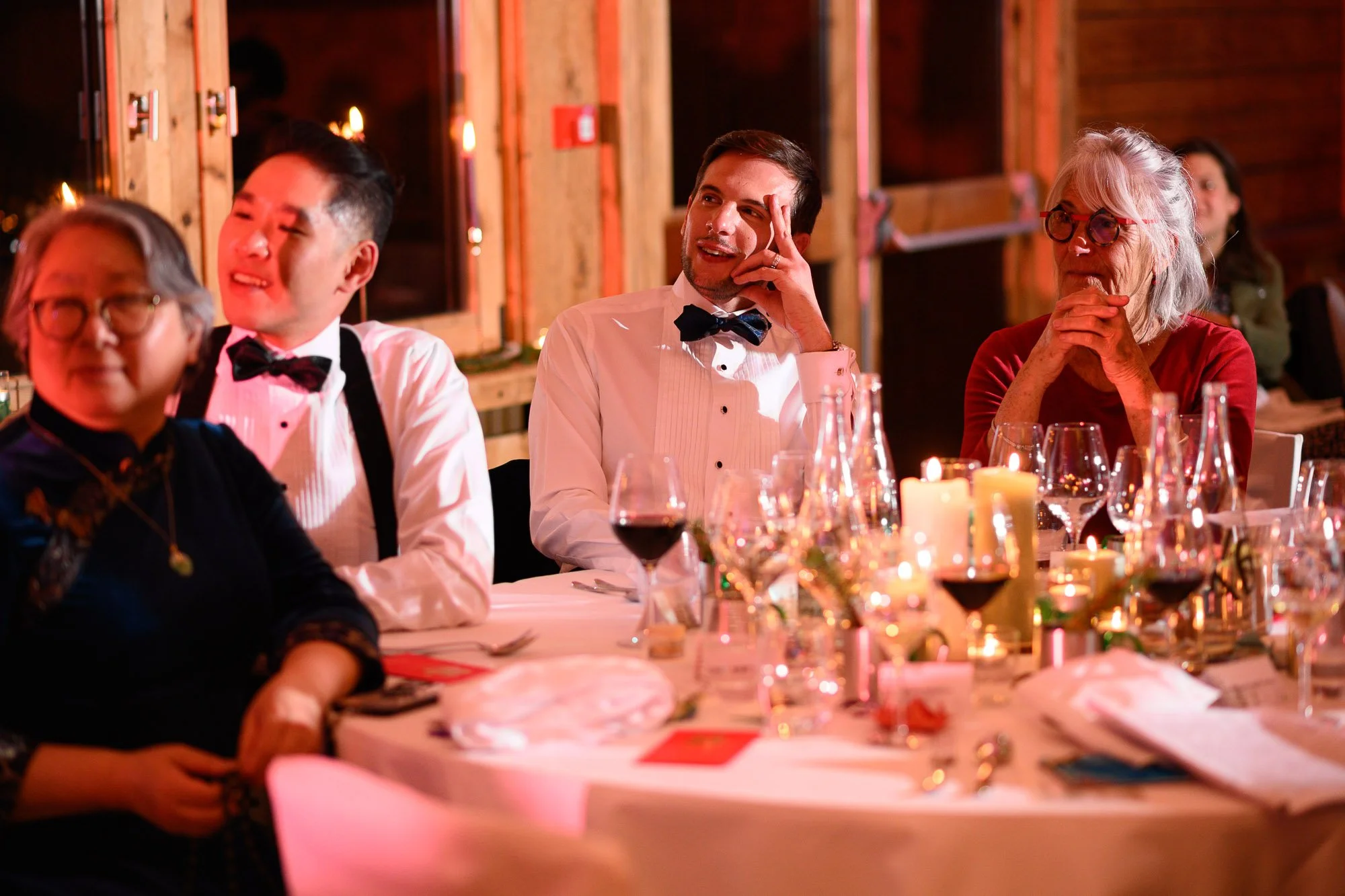 Groupe de personnes assises à une table lors d'un dîner élégant, en tenue formelle, entourée de bougies et de décorations de fête dans une ambiance chaleureuse.