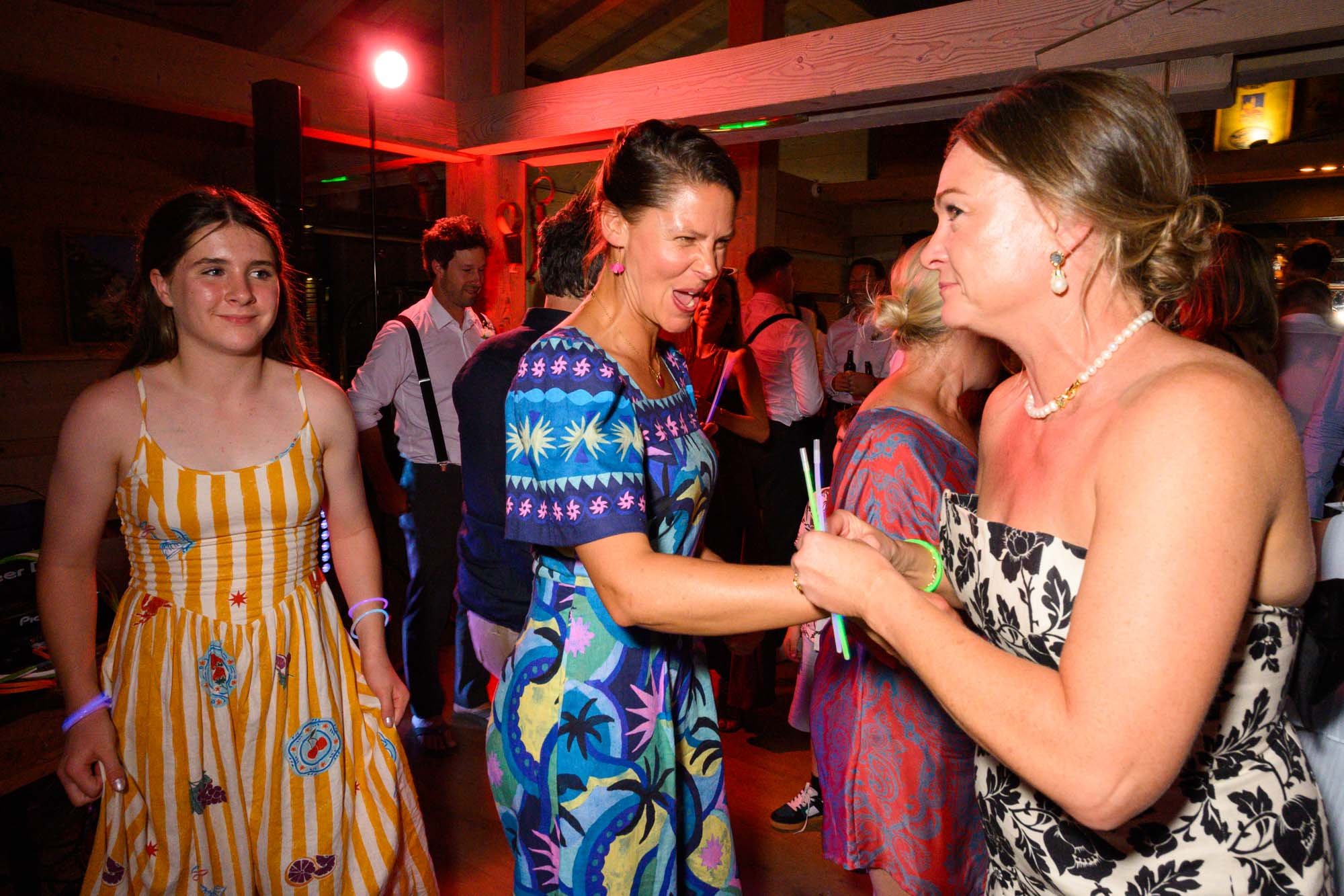 Une femme en robe noire et blanche serrant la main d'une autre femme en robe colorée lors d'une fête dans une ambiance chaleureuse.