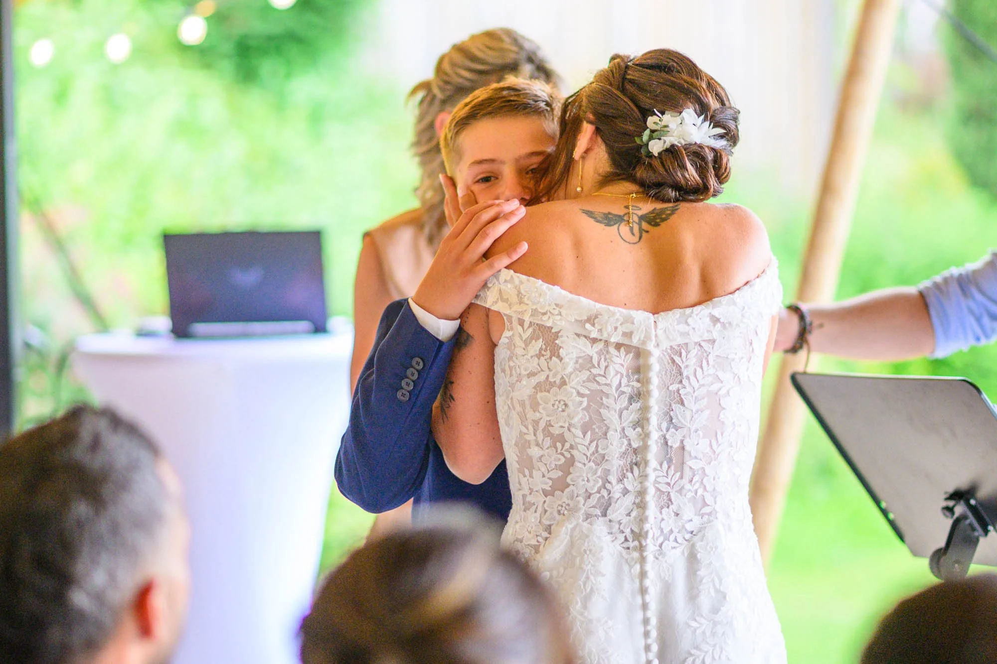 Une femme en robe de mariage et un jeune homme en costume s'embrassent lors d'une cérémonie de mariage en plein air.