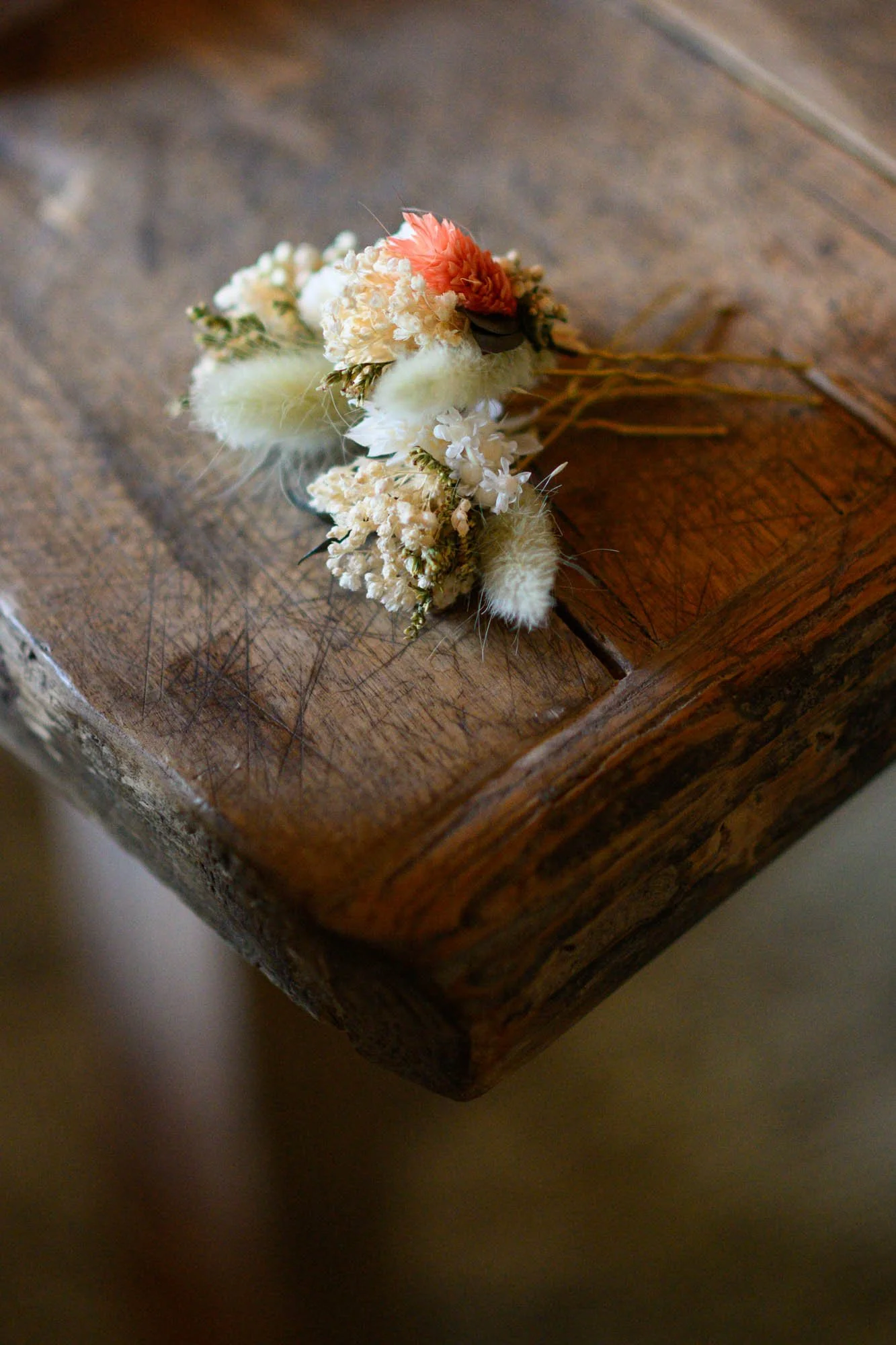 Petite composition florale composée de fleurs blanches, roses et de plumes, posée sur une surface en bois.