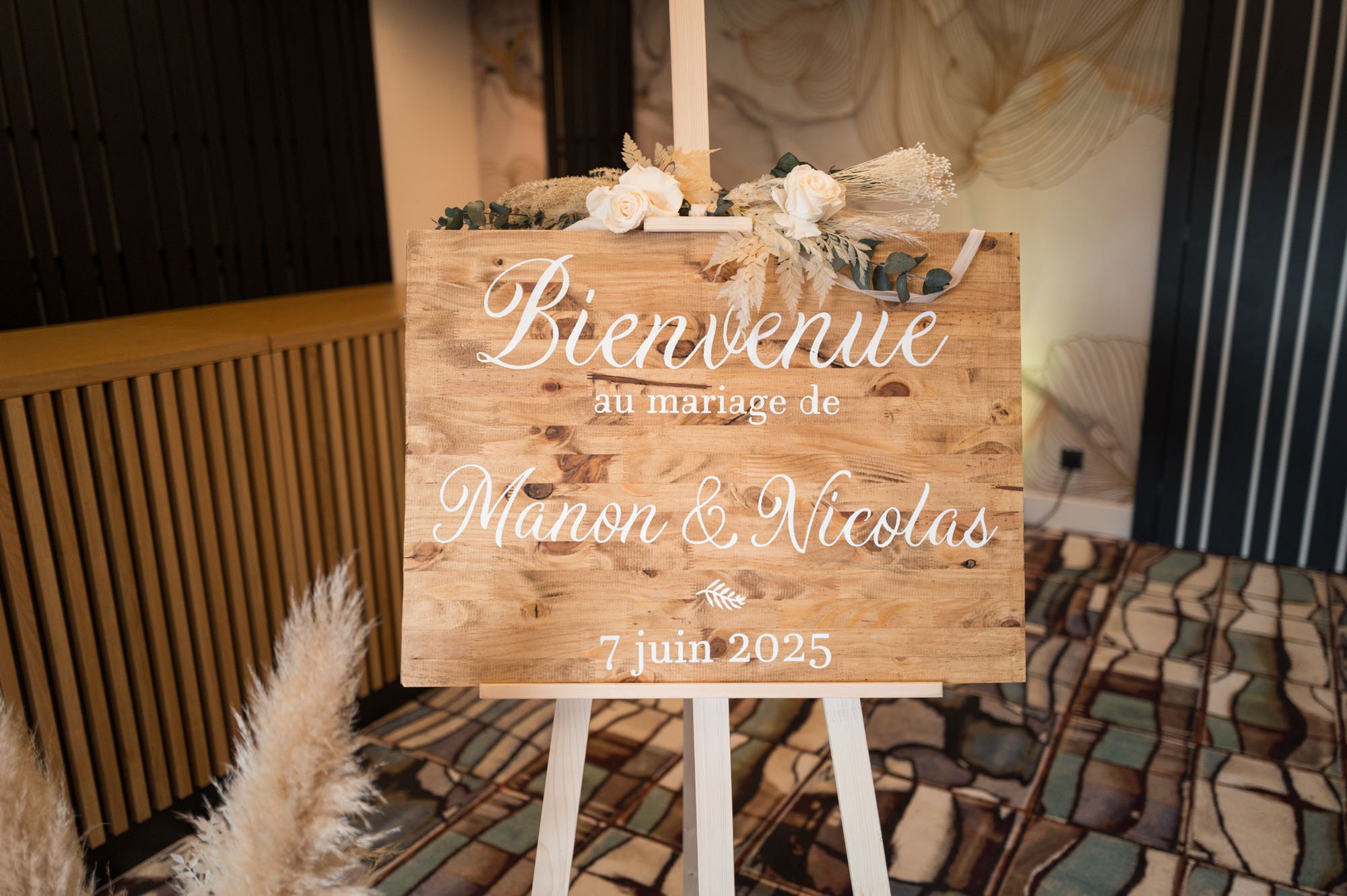 Panneau en bois avec message d'accueil écrit en français pour un mariage, décoré de fleurs, sur un support en bois, date 7 juin 2025.
